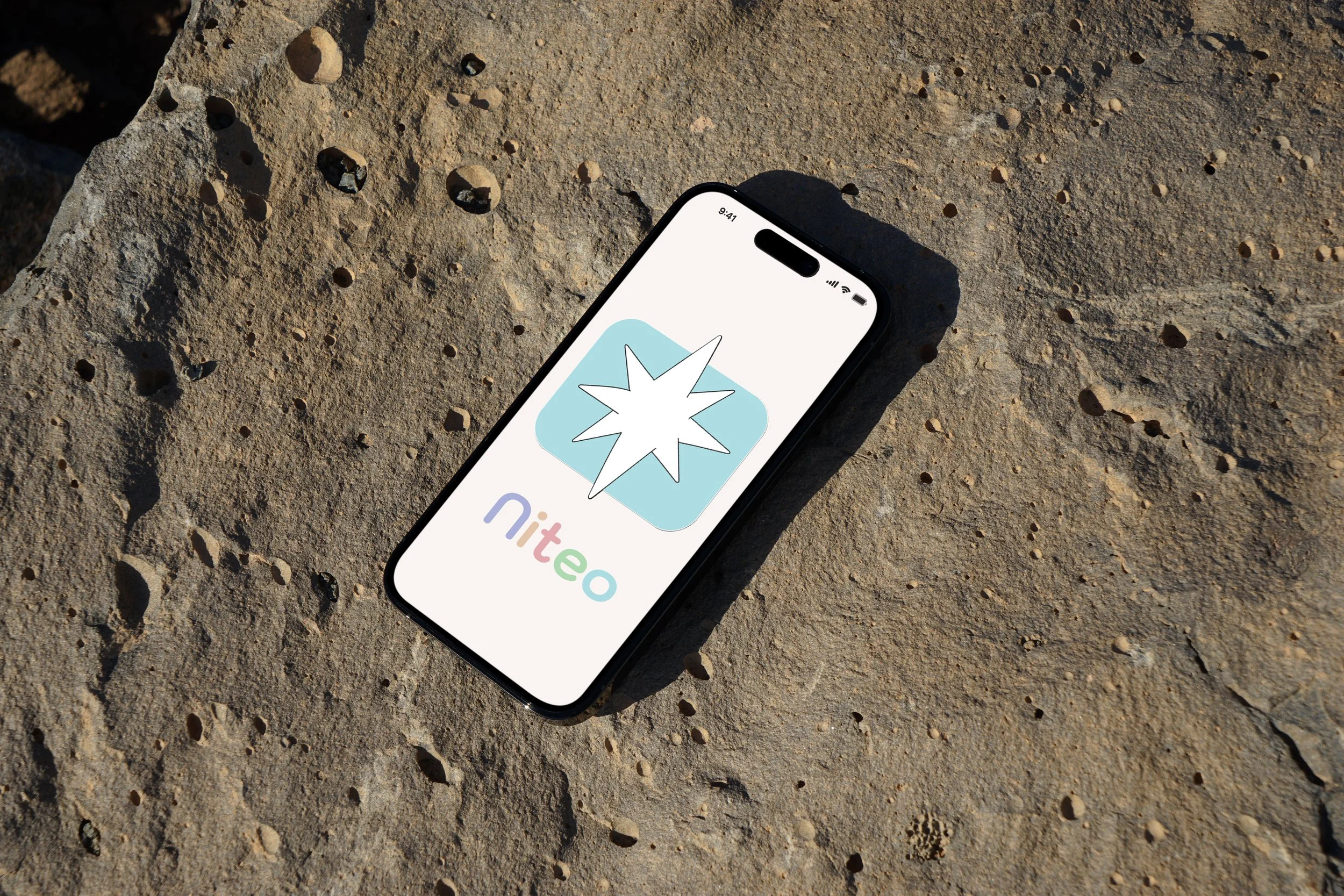 Smartphone lying on sandy ground displaying the Niteo app logo with a stylized star burst icon.
