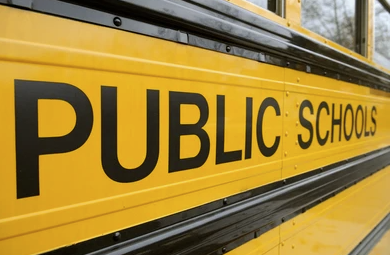 Close-up of the side of a yellow school bus with the words "PUBLIC SCHOOLS" written in black.