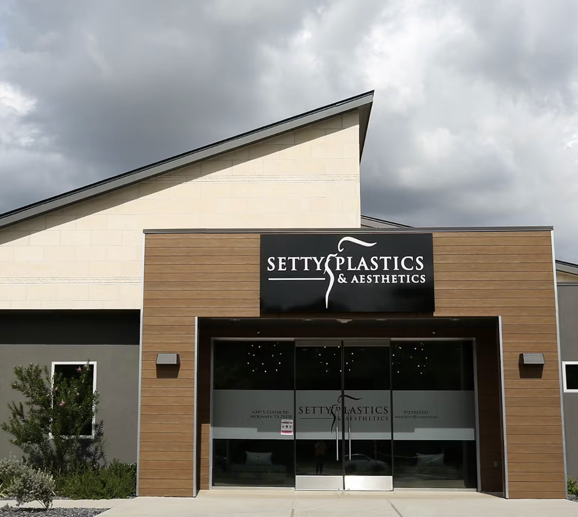 Front view of a beauty clinic named Setty Plastics & Aesthetics with a black signboard, large glass doors, and modern exterior design with wood and neutral-colored walls.