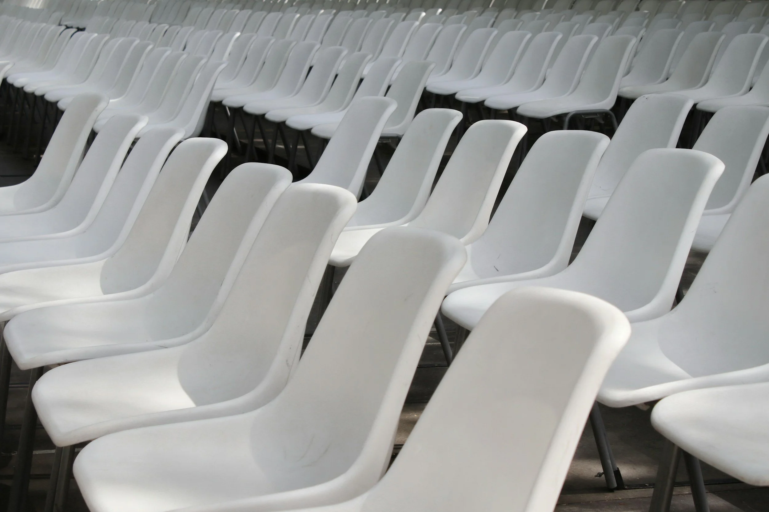 Multiple white plastic chairs arranged in rows in an indoor venue.