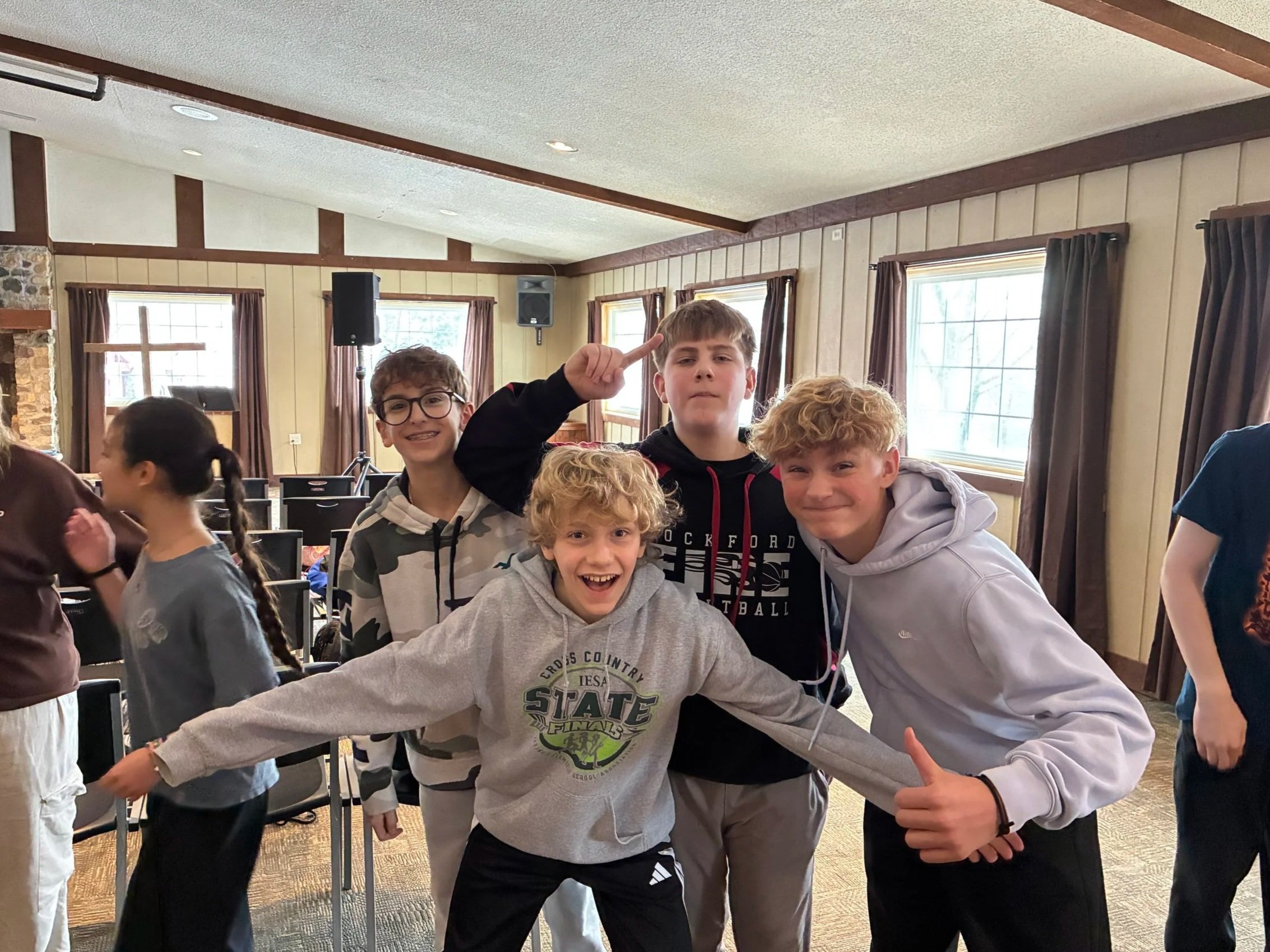 Group of five boys happy and posing for camera inside a room with wooden walls and large windows.