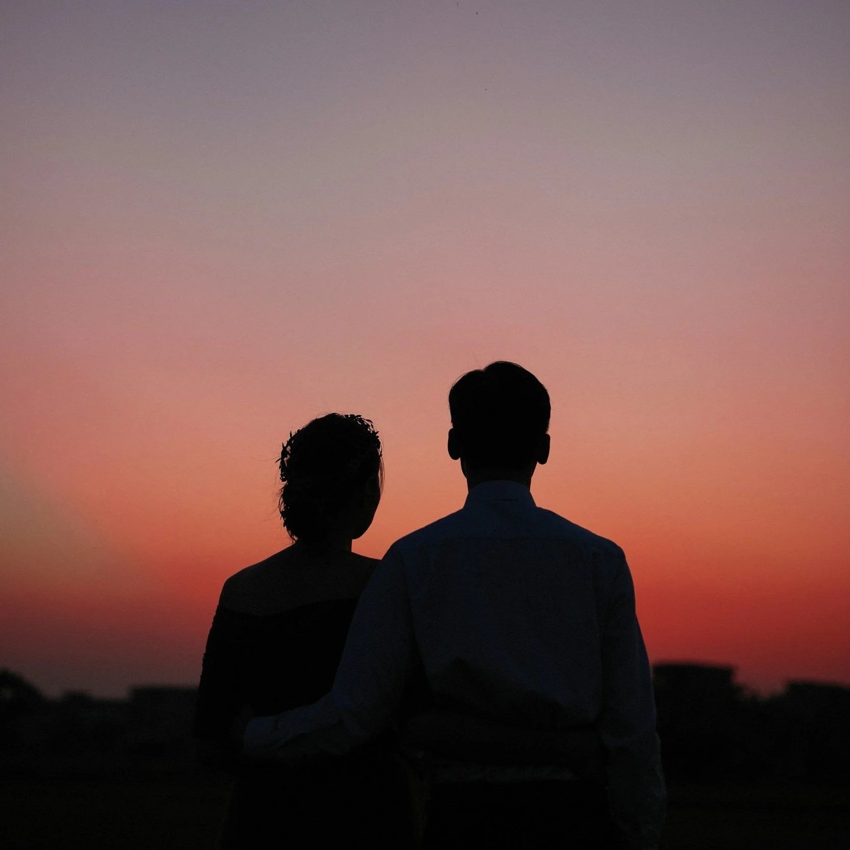 Silhouettes of a man and woman standing together outdoors during sunset or sunrise.