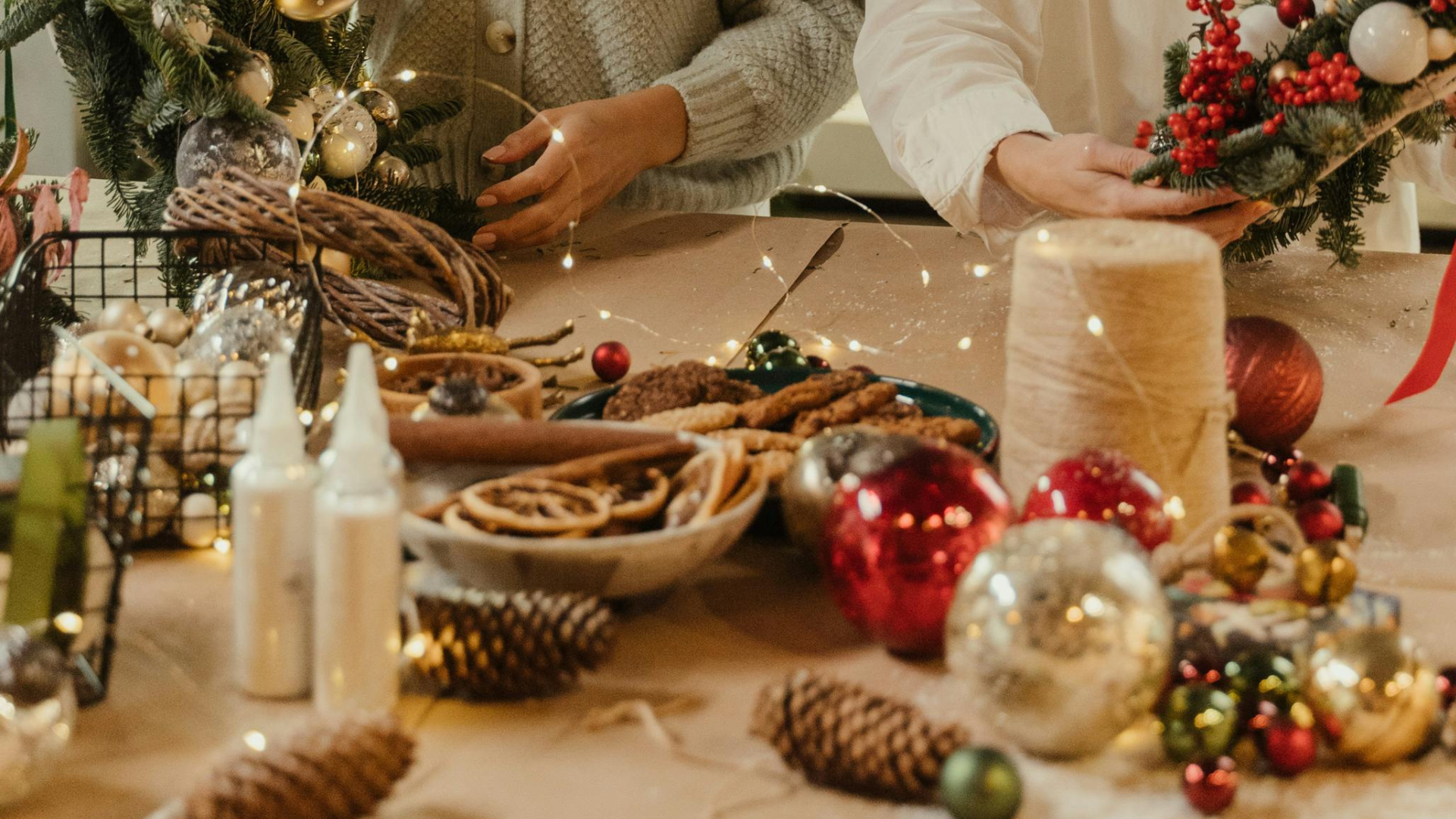 People decorating a table with Christmas ornaments, pinecones, cookies, and holiday decorations.
