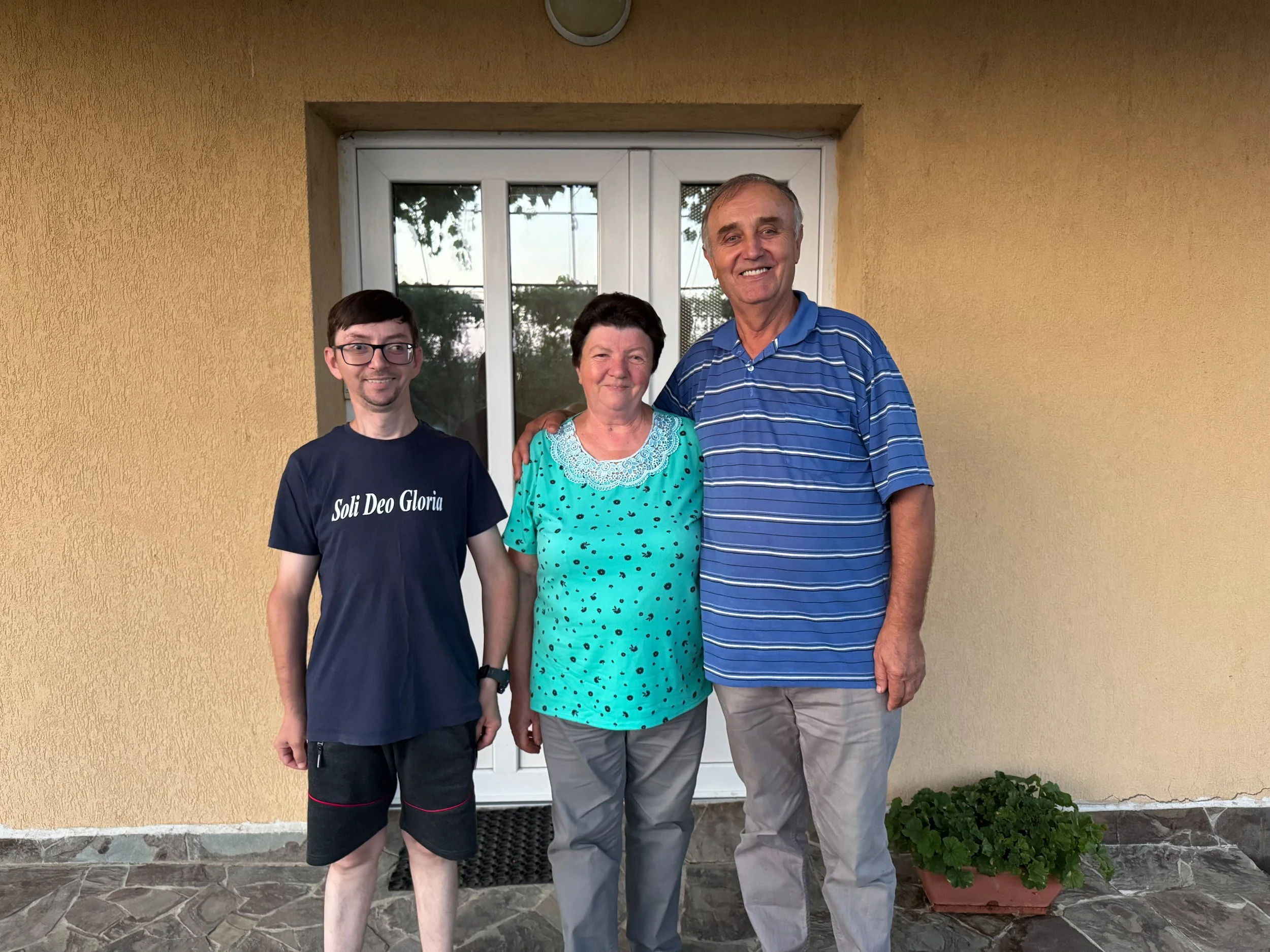Three people standing in front of a yellow wall and a glass door, smiling and posing for a photo.