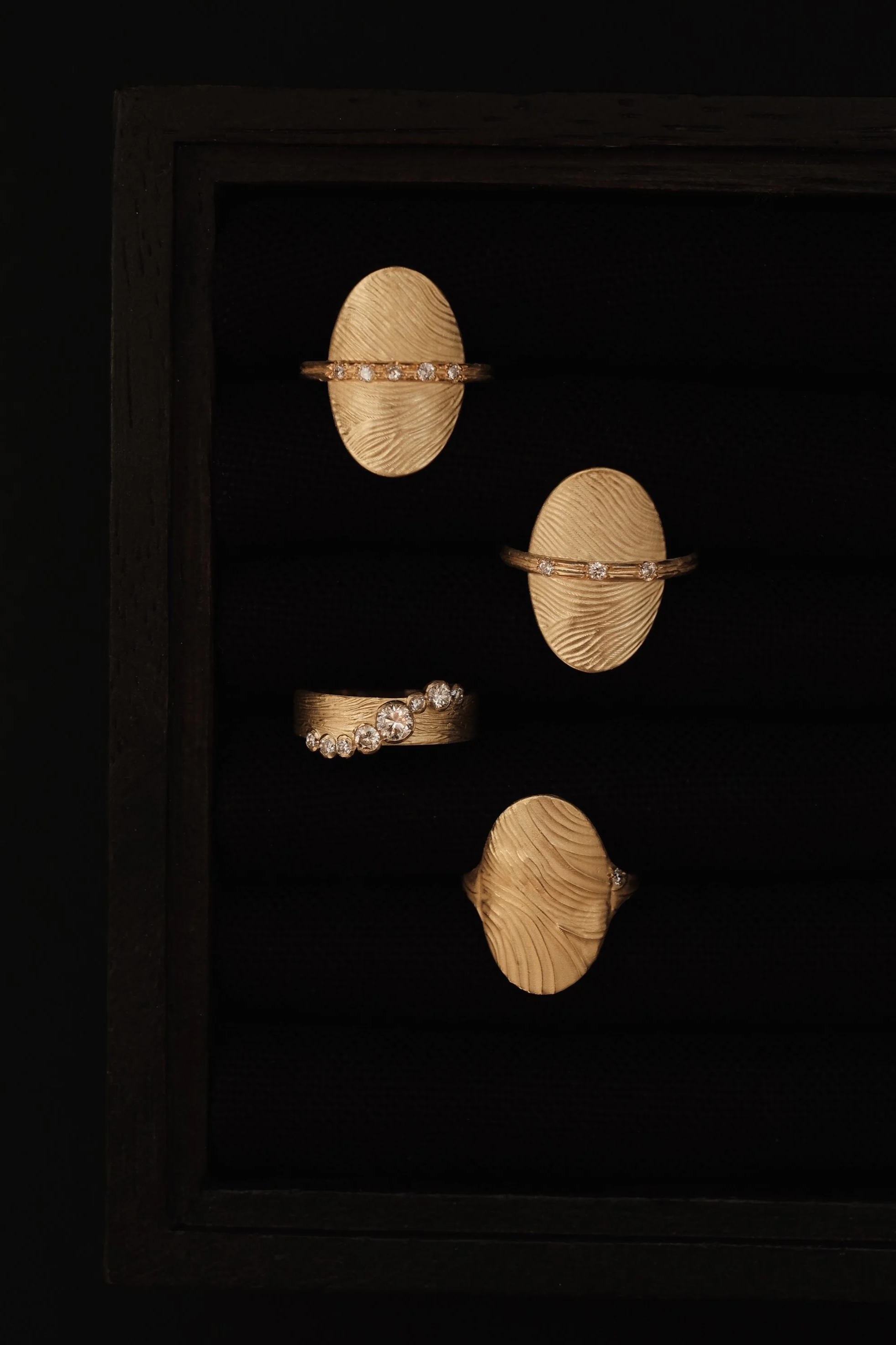 Collection de bijoux en or ornés de diamants, comprenant deux bagues, exposés sur des supports en forme d'empreinte digitale, dans une vitrine noire en bois.