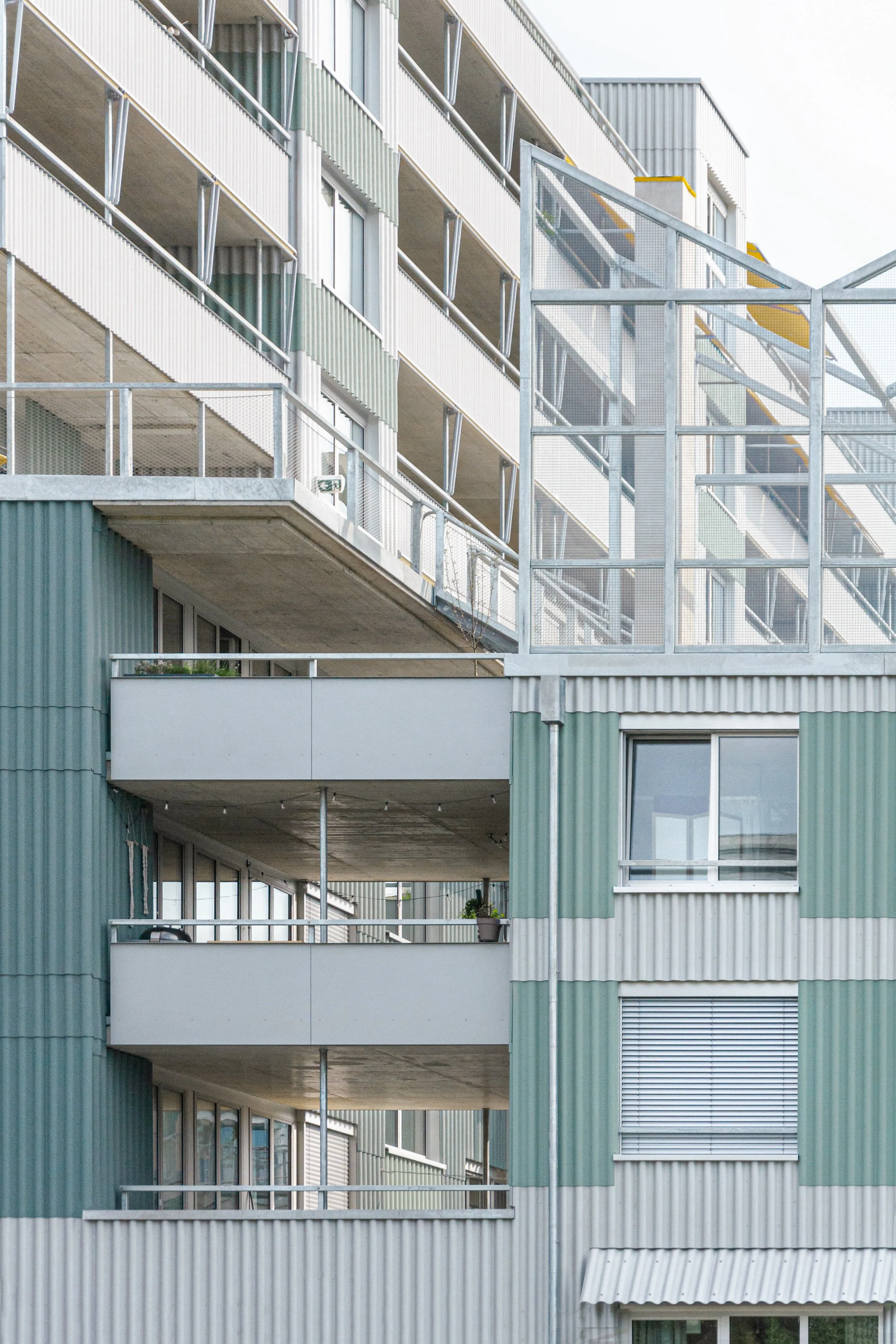 Close-up of modern apartment building with multiple balconies, large windows, and metal railings, featuring a green and white color scheme.
