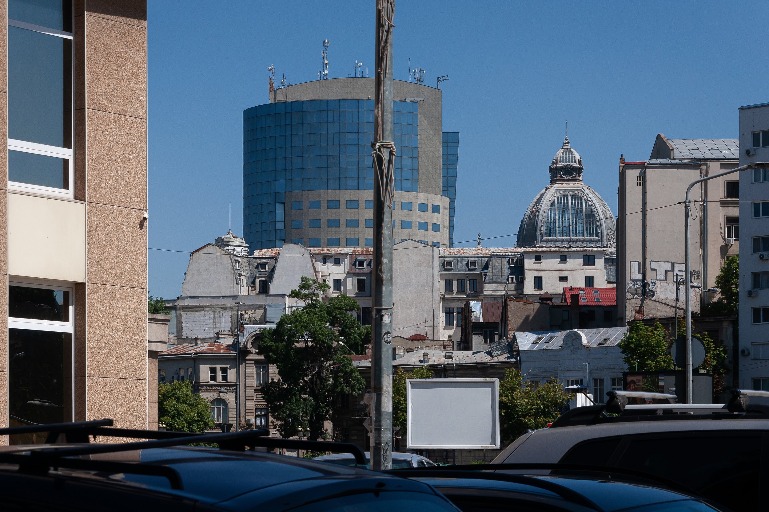 Cityscape with modern glass building and historic domed structure in the background, parking lot in the foreground.