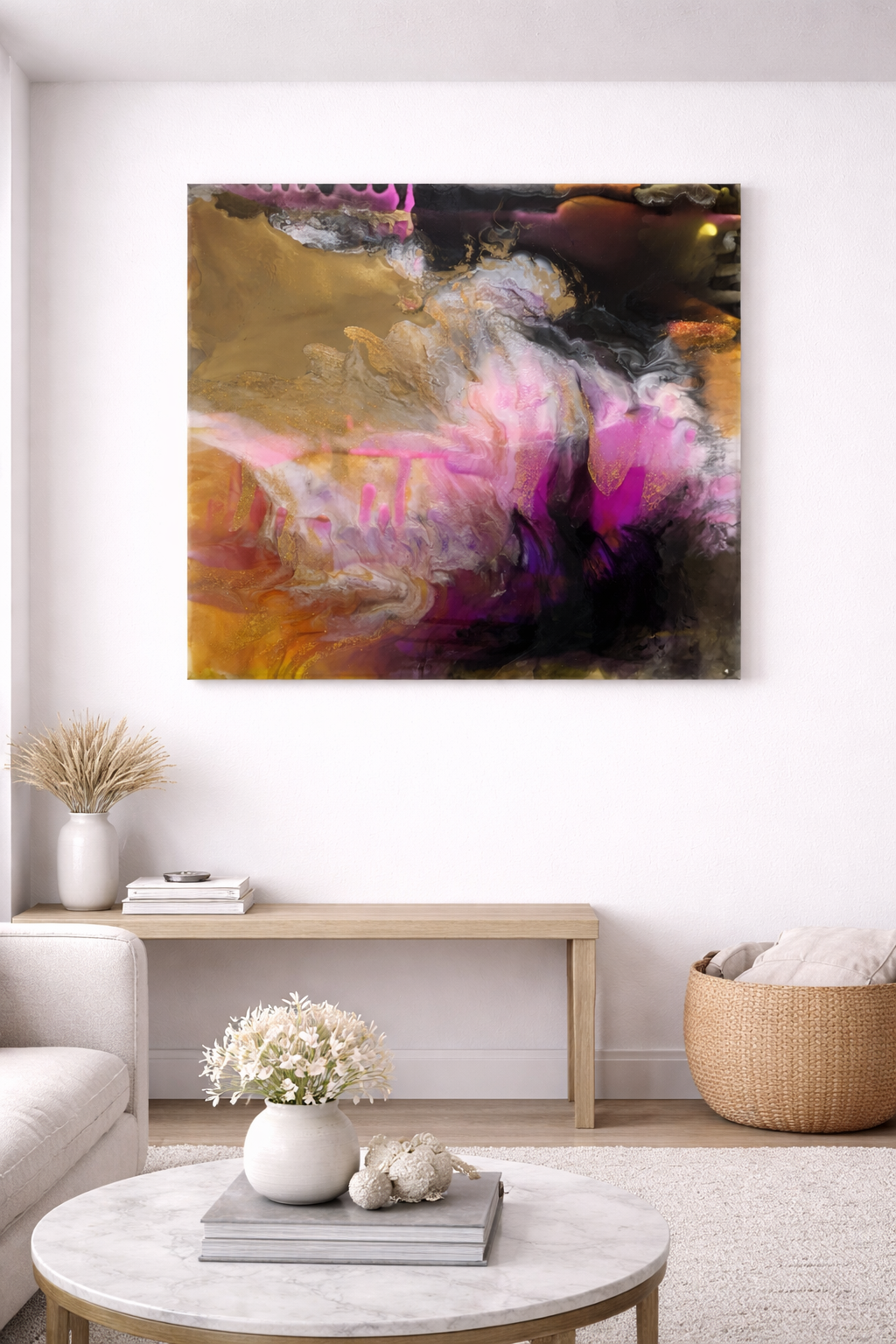Abstract art painting with pink, purple, black, gold, and white swirls hanging on a white wall in a modern living room with a beige sofa, a round marble coffee table with a white vase of flowers, and a woven basket.