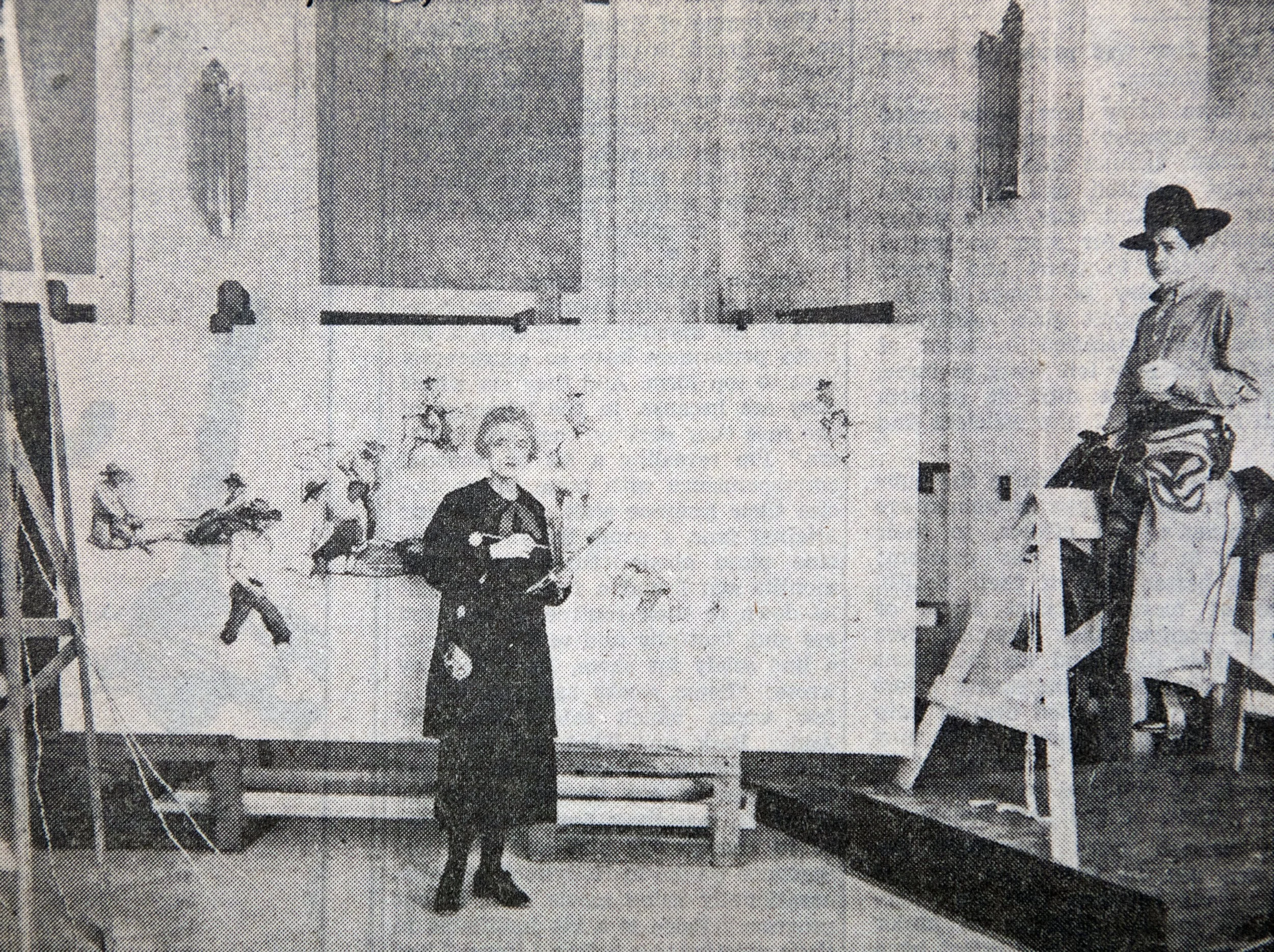 Black and white photograph depicts Ruth Monro Augur standing in front of an easel with one of her WPA murals.