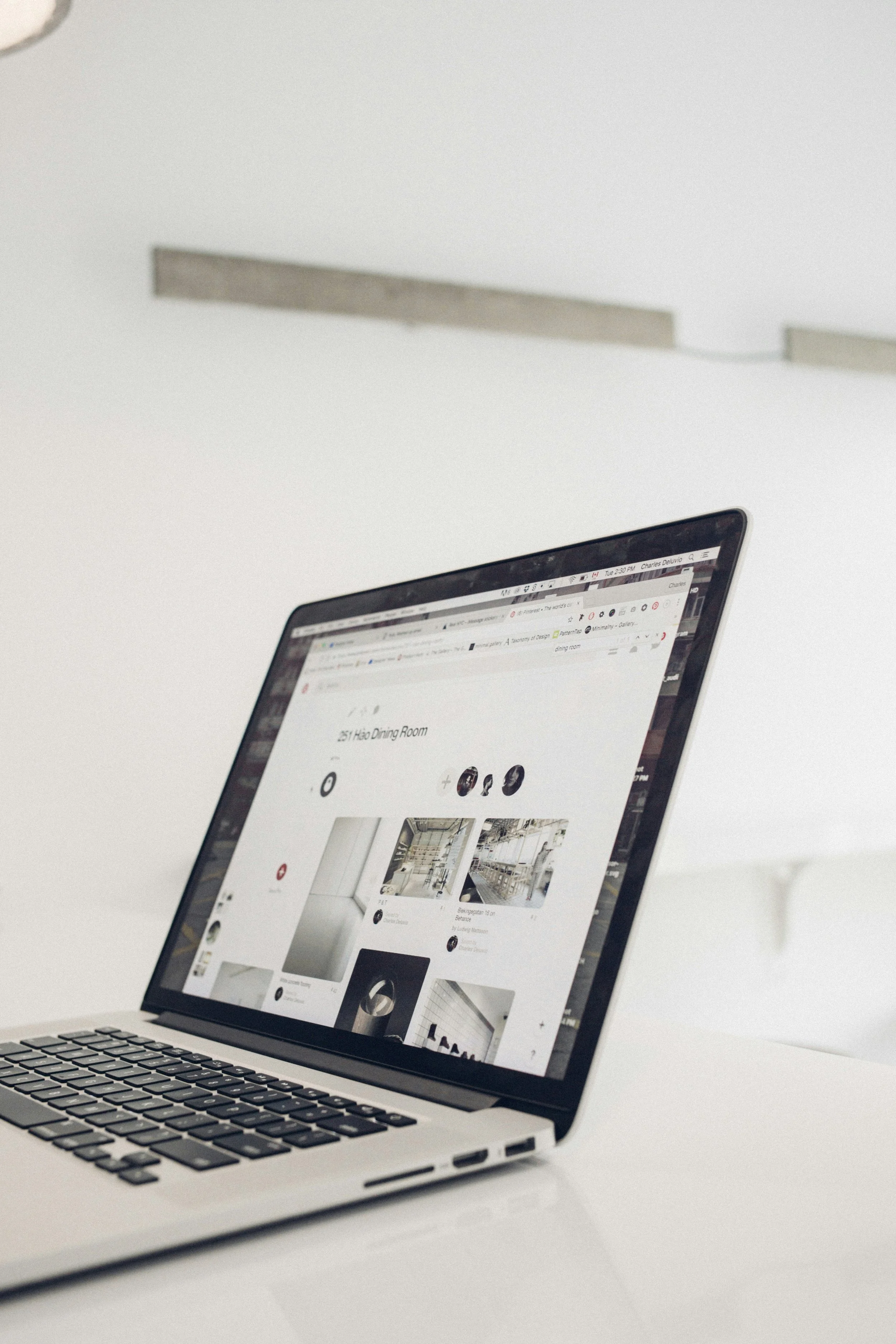A silver MacBook laptop on a white desk, displaying a webpage with images of modern interior design and a title '251 Hao Dining Room'.
