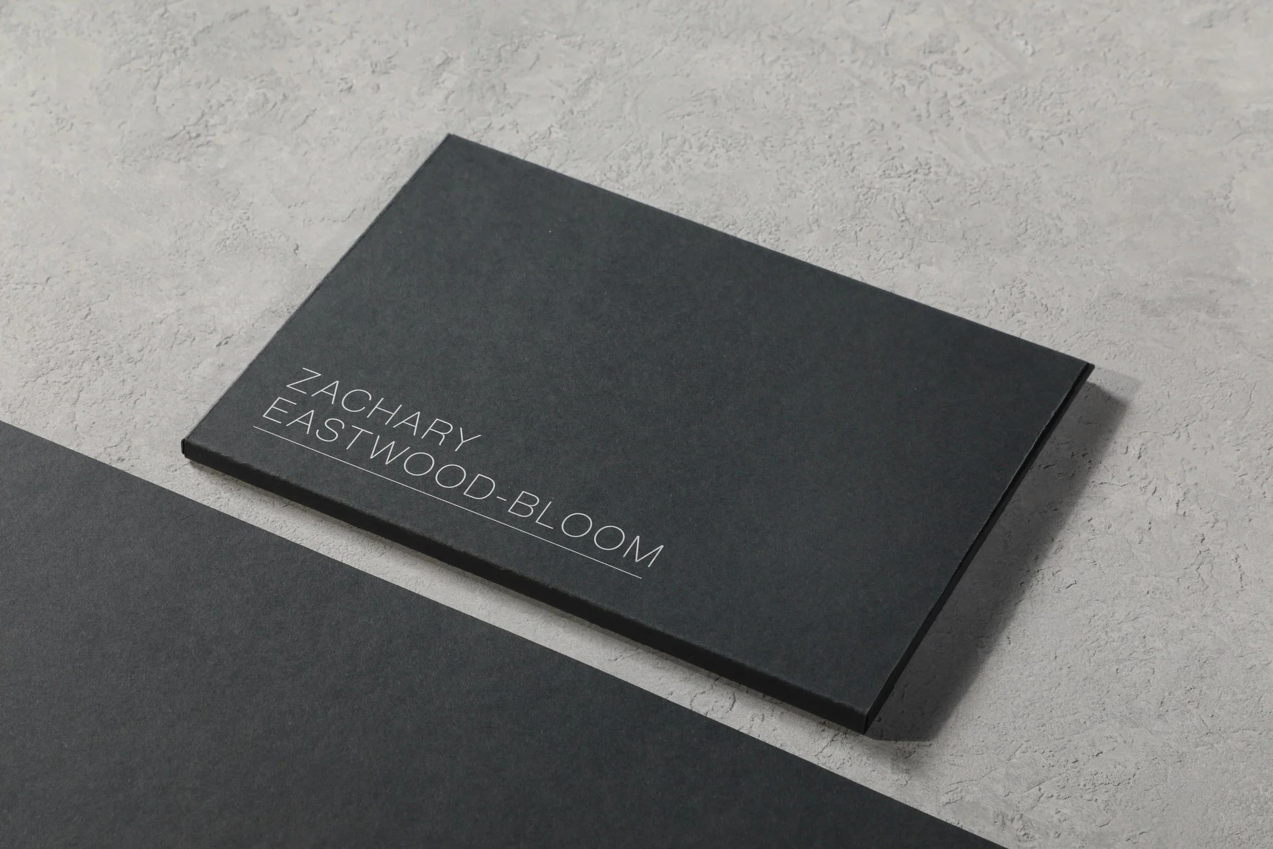 A black rectangular box with white text reading 'Zachary Eastwood-Bloom' on a textured light gray surface.