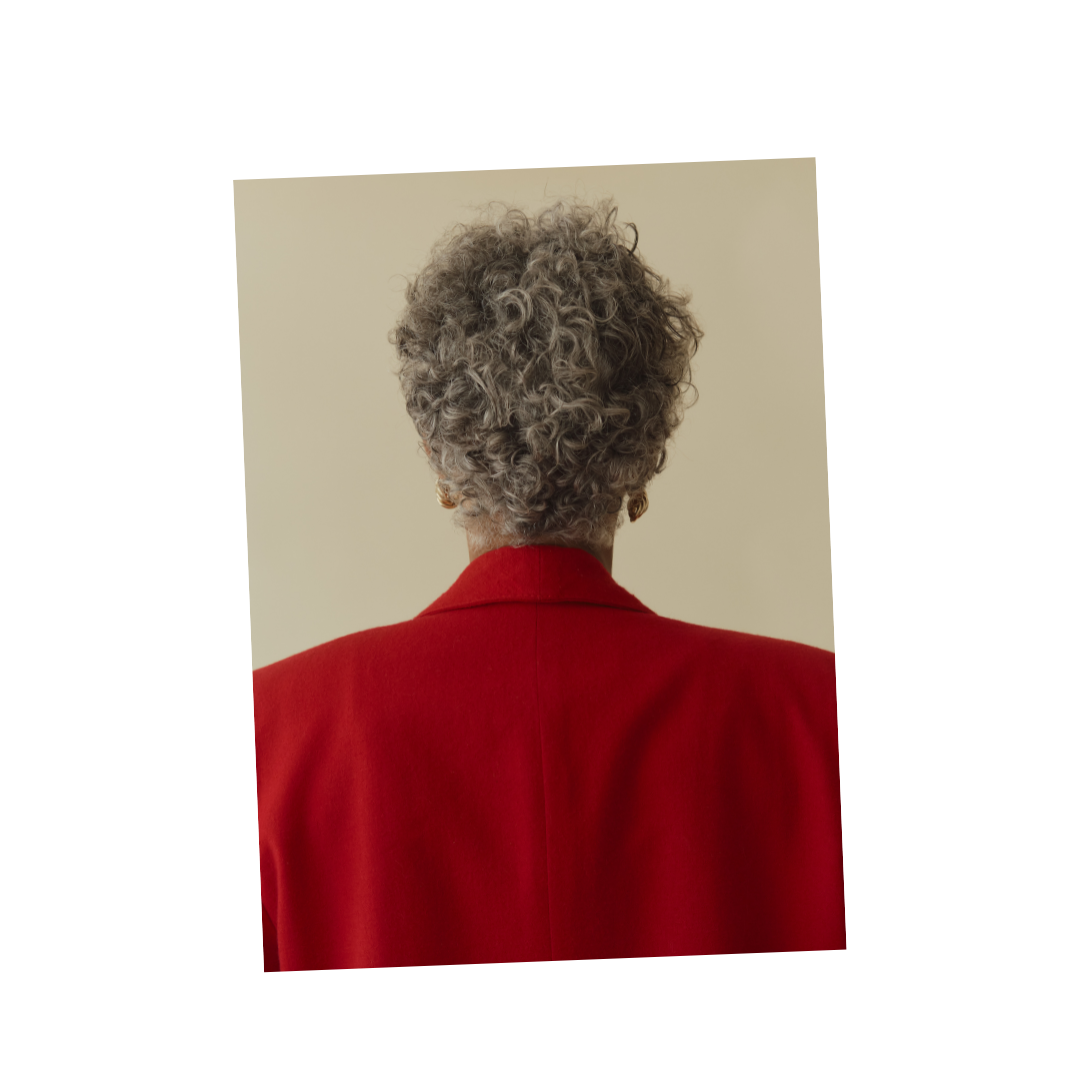 Back view of an elderly person with gray curly hair wearing a red blazer.