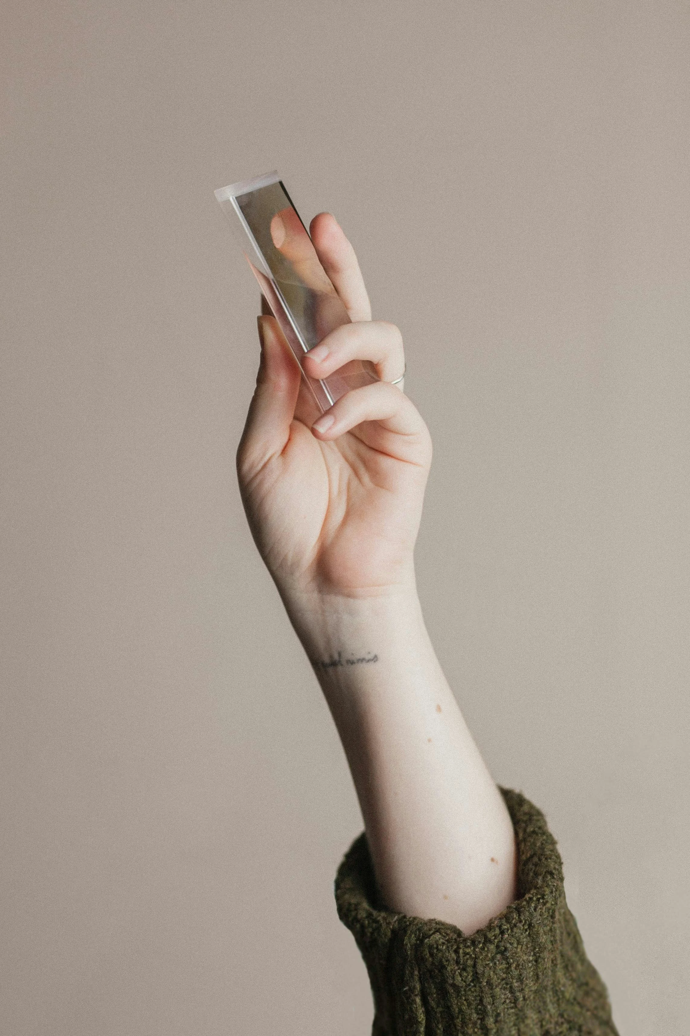 A person holding a smartphone with a blurred photo, wearing a brown knitted sweater, with a small tattoo on the wrist.