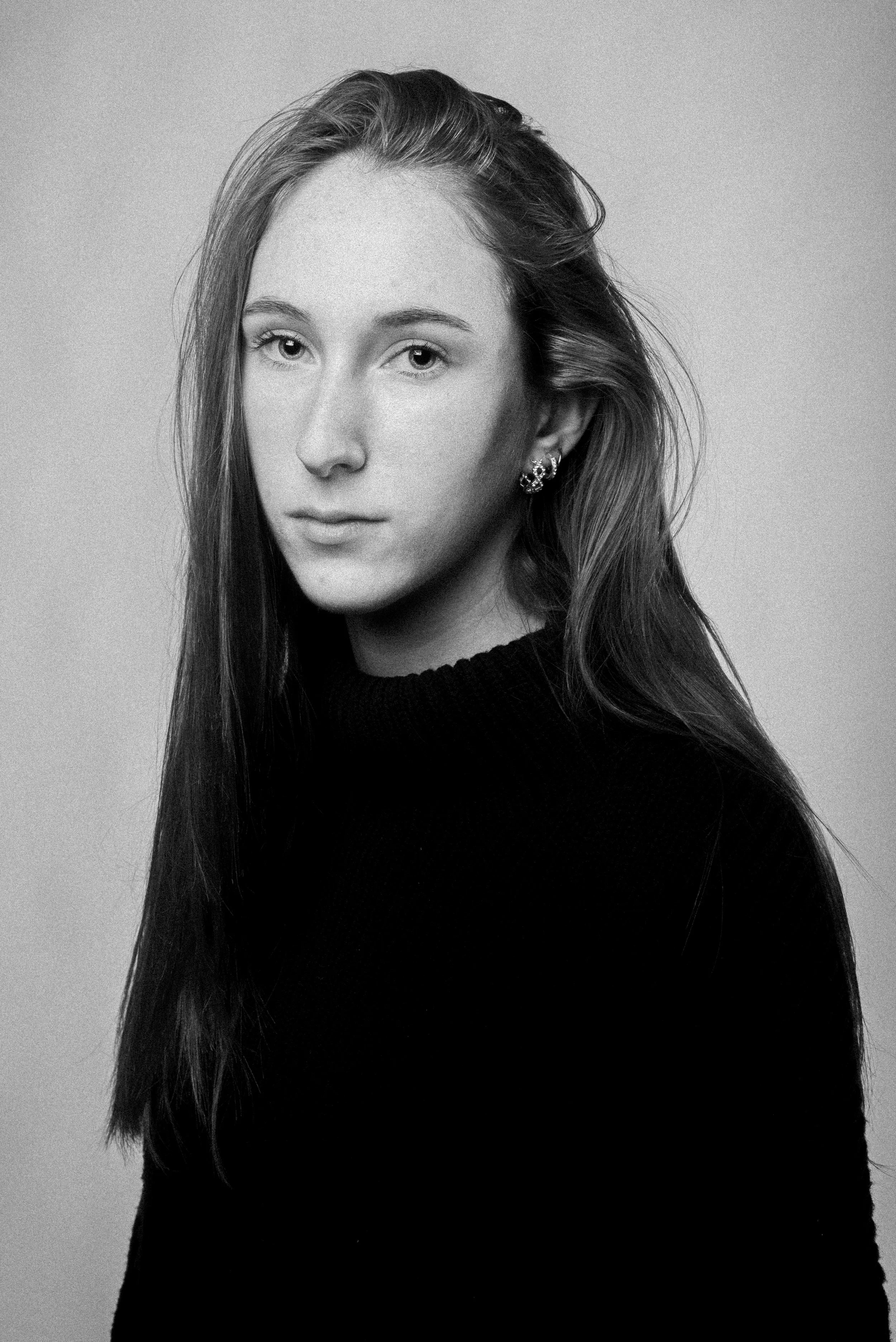 Black and white portrait of a young woman with long hair wearing a black turtleneck and earrings.