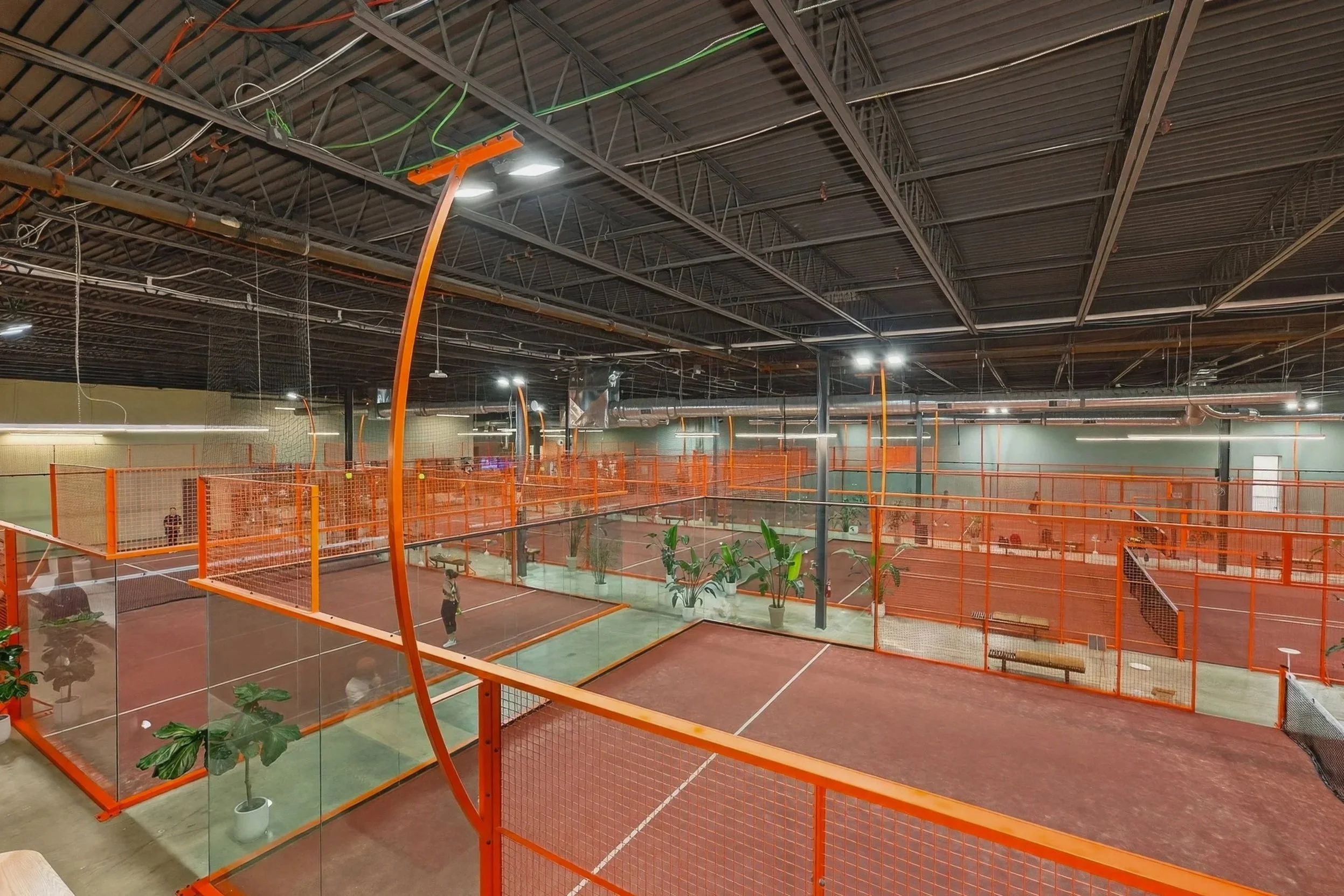 Large house with a brick and wood exterior, a sloped roof, and a stone foundation. It has multiple windows, a rounded balcony, and an outdoor seating area with small tables and chairs in the yard.