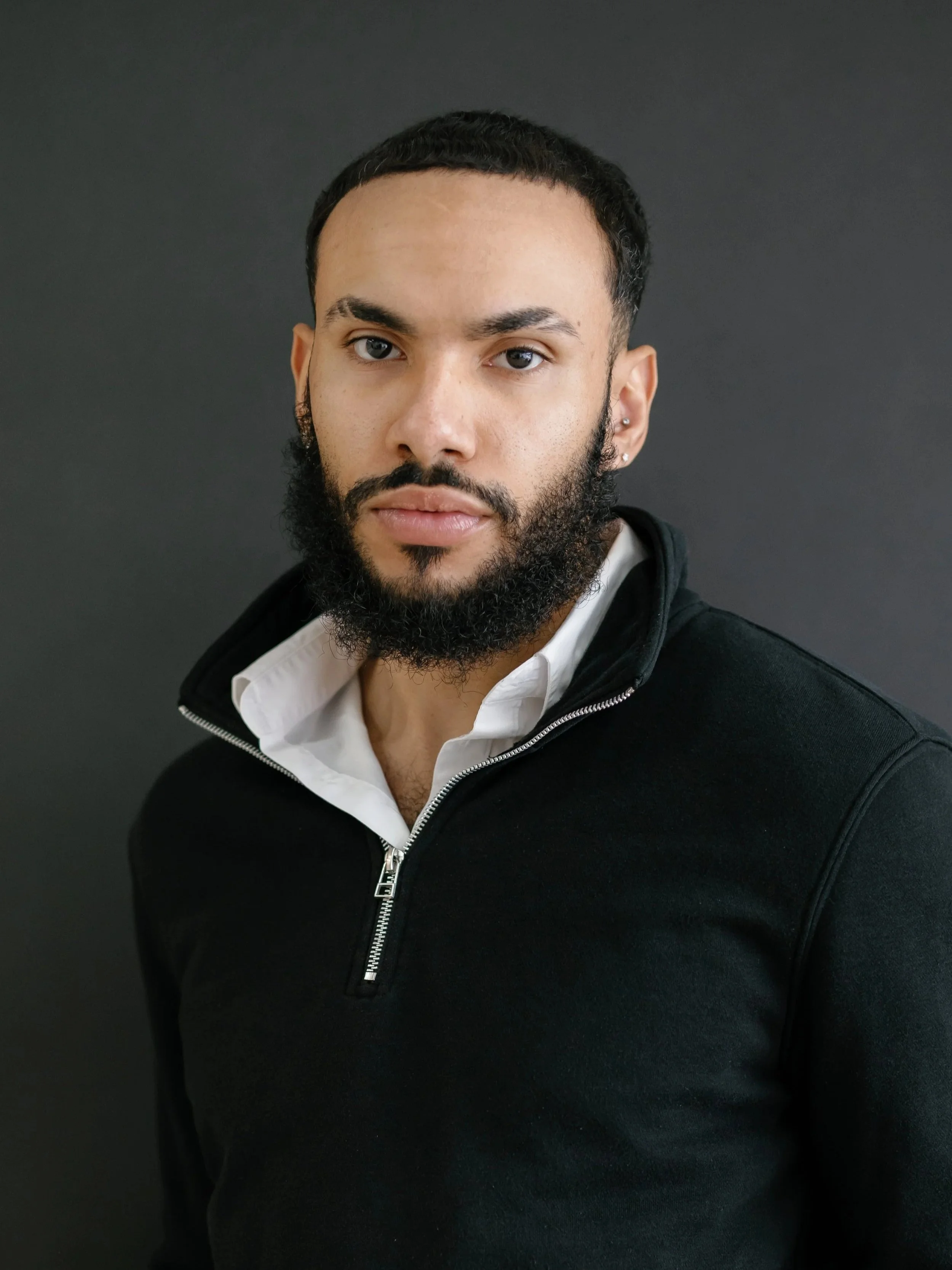 A man in a blue suit and yellow tie standing outdoors in front of a brick building and green grass.