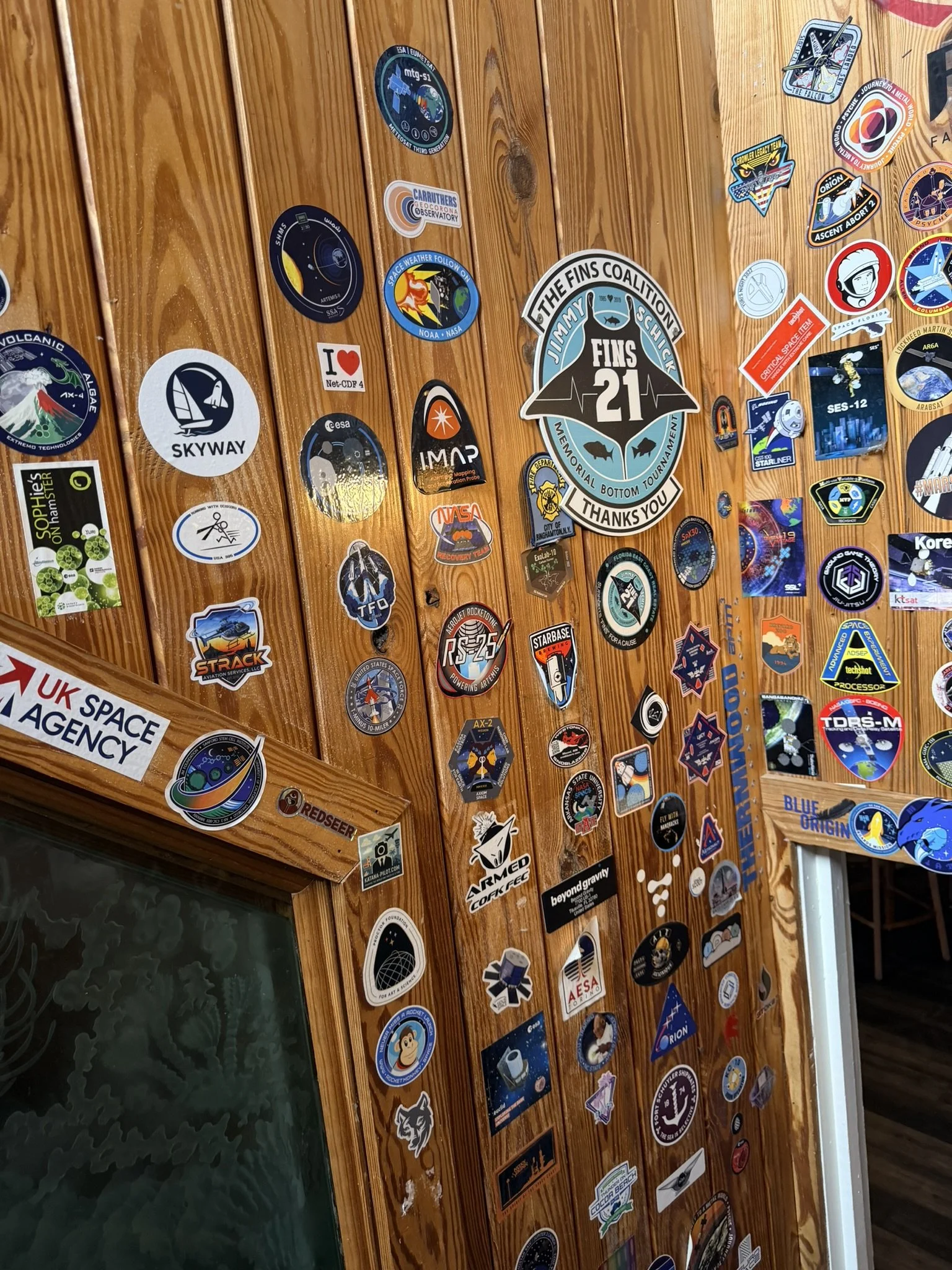 A paneled wall covered with a myriad of mission patch stickers.