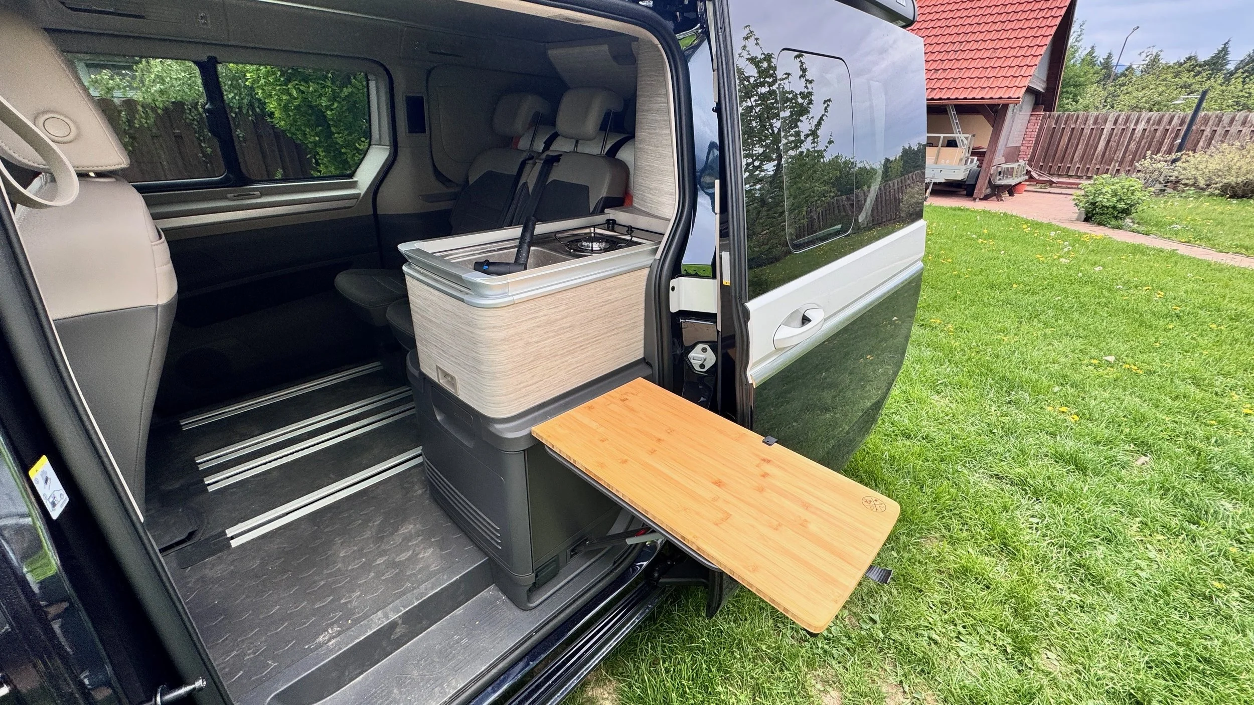 The interior of a camper van with a fold-out wooden table, a small kitchen area with a sink and stove, and seating area with seats facing each other.