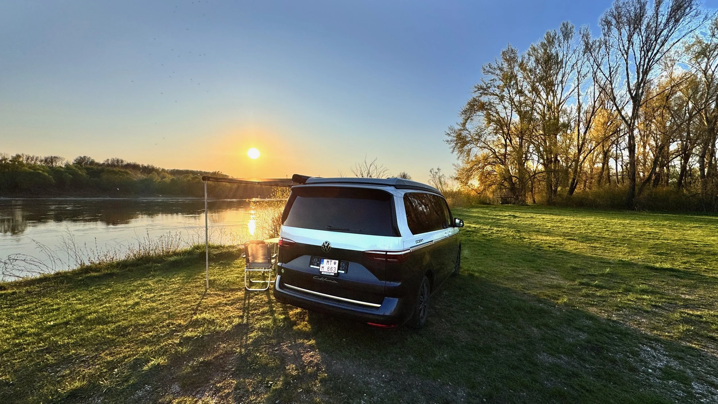 Volkswagen California camper zaparkovaný pri rieke počas západu slnka