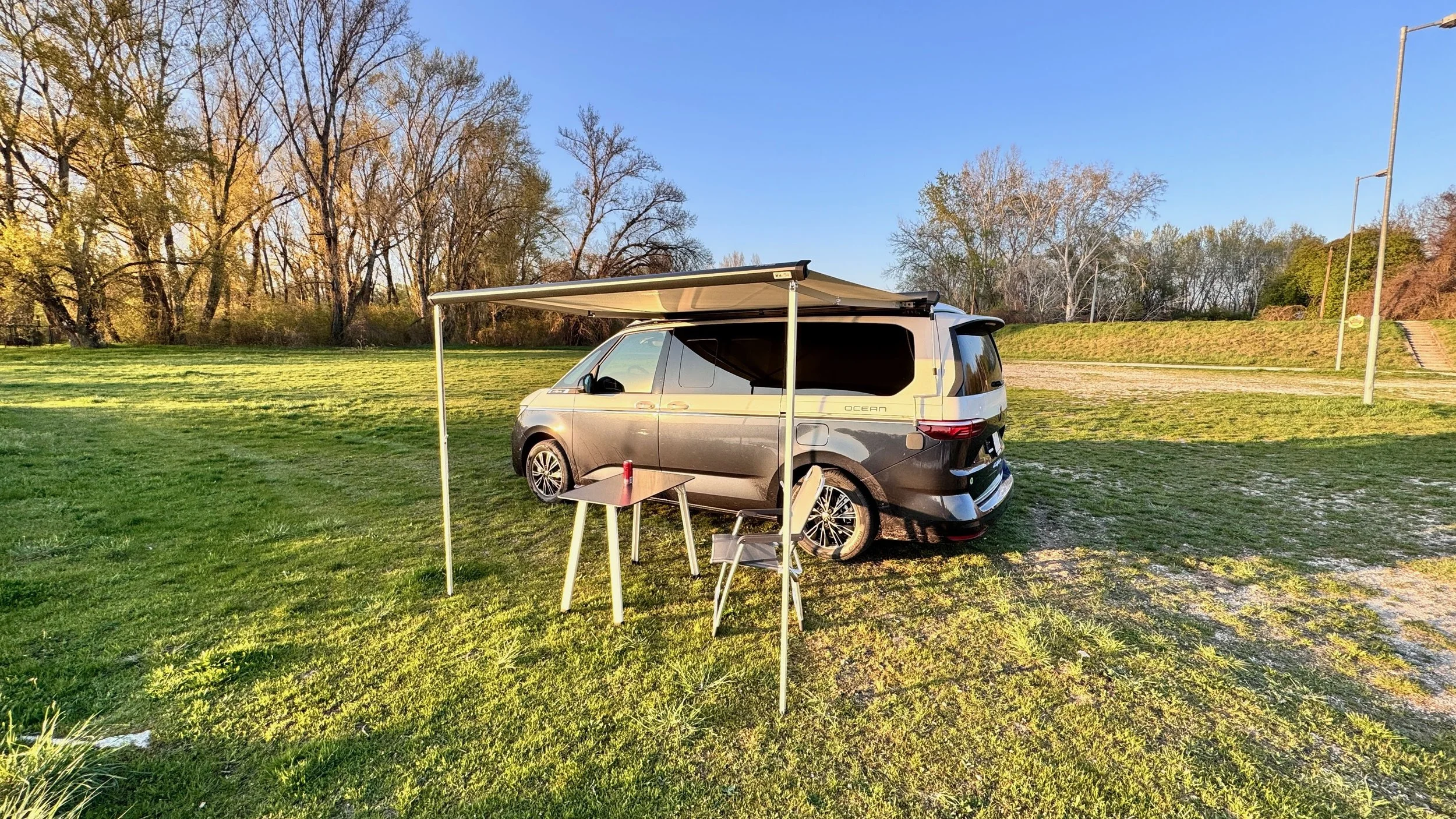 VW California s rozloženou markízou a kempingovým stolom na lúke