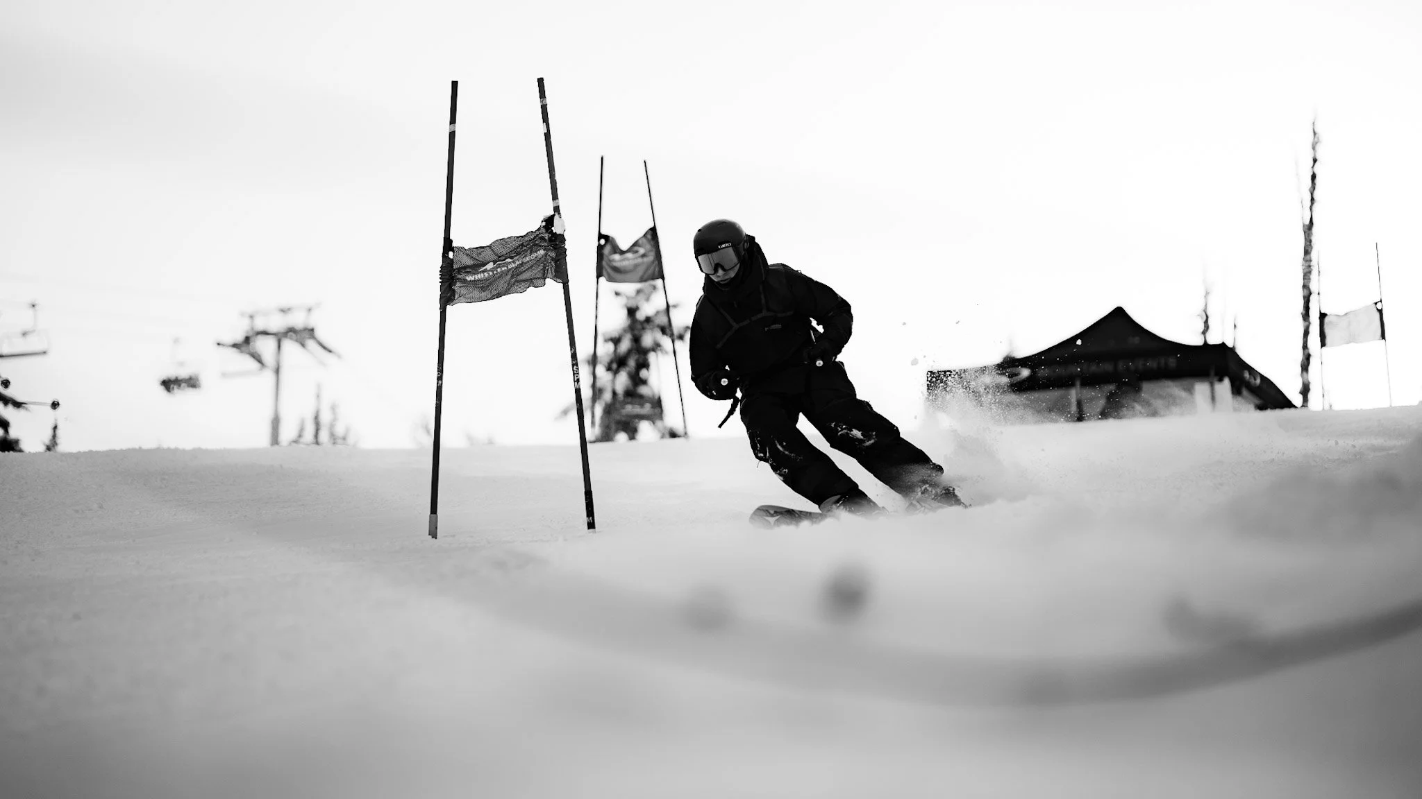 A skier descending a snowy slope, navigating around gate poles during a race or training session in a mountain area, with ski lift equipment and a building in the background.