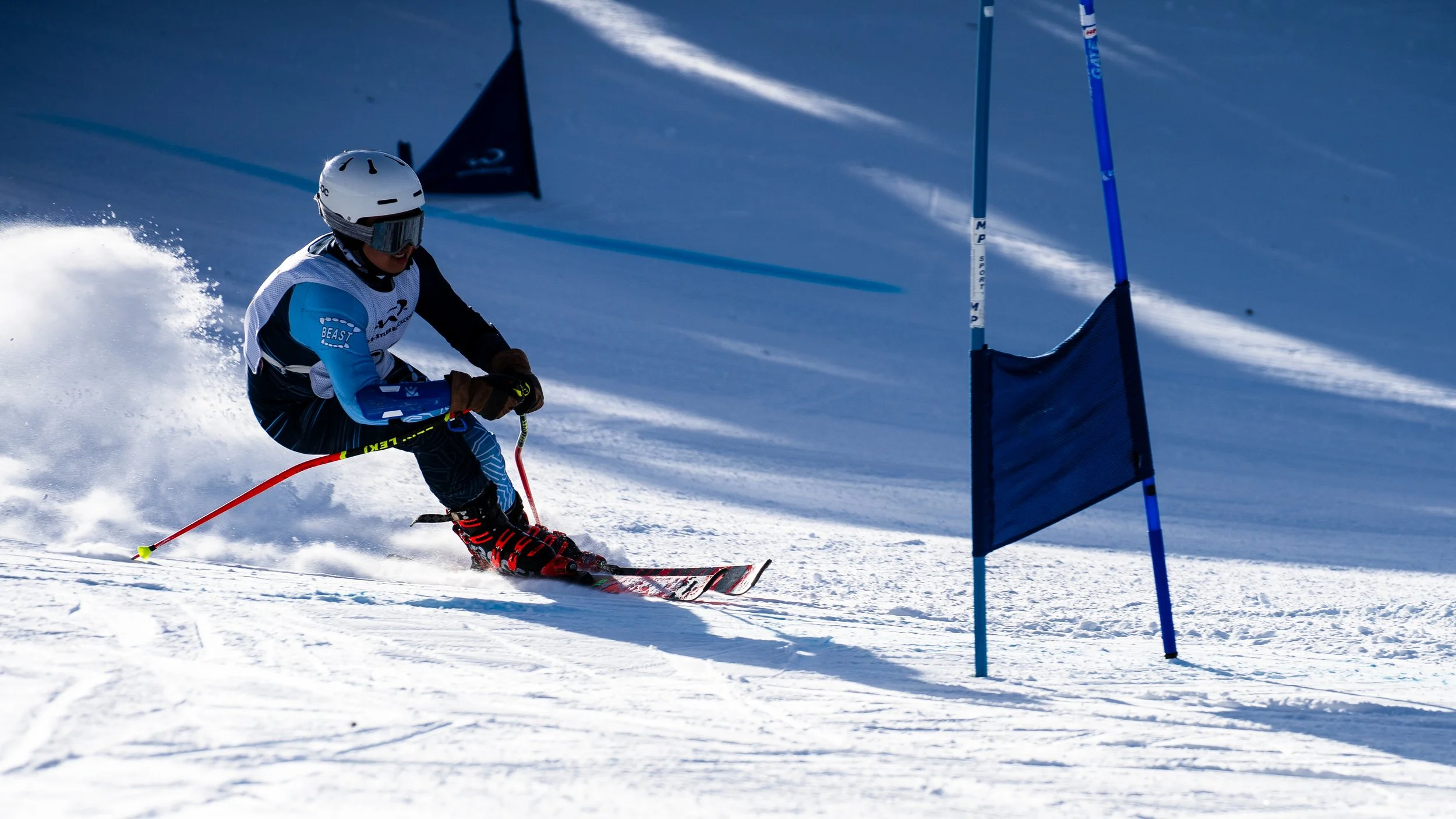 A skier in a blue and black outfit, wearing a white helmet and goggles, navigating a slalom course on a snowy mountain slope with blue gate flags.
