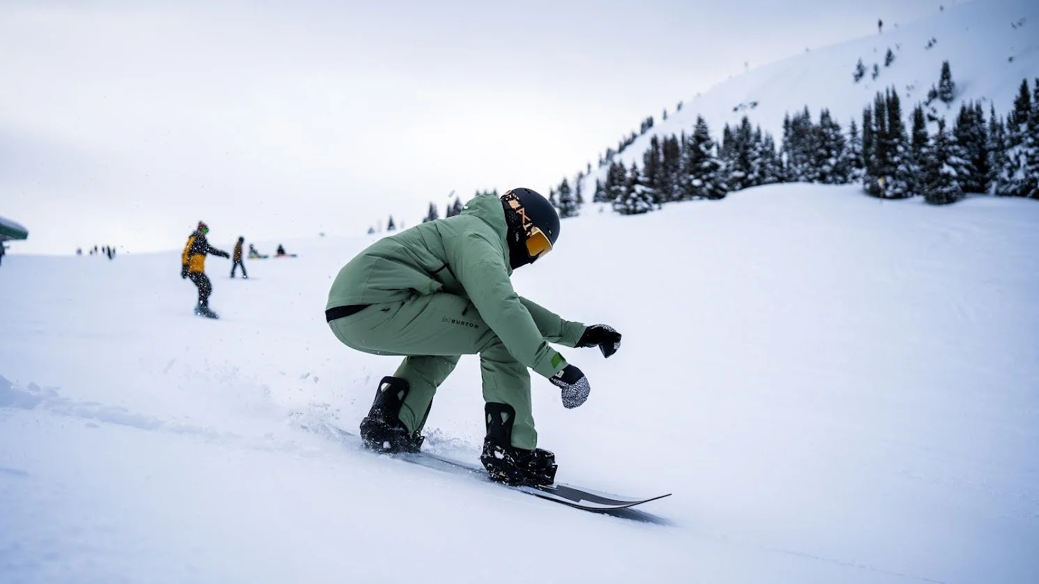 A person wearing a green outfit and black helmet snowboarding on a snowy mountain slope.