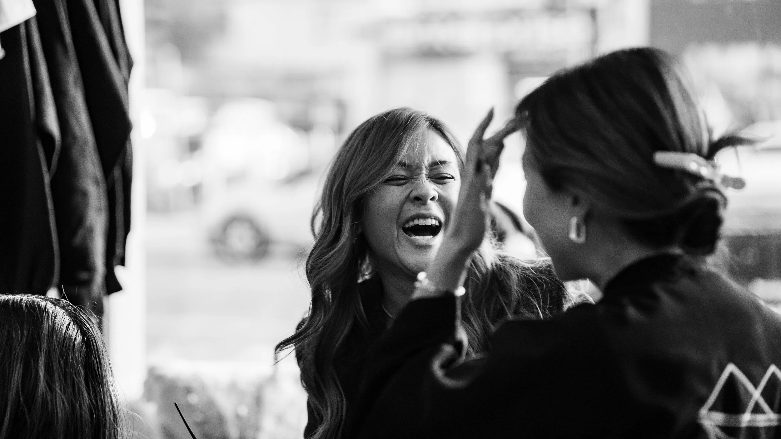 A woman with long hair appears to be upset or upset with another woman near a window, with her hand raised near her head.