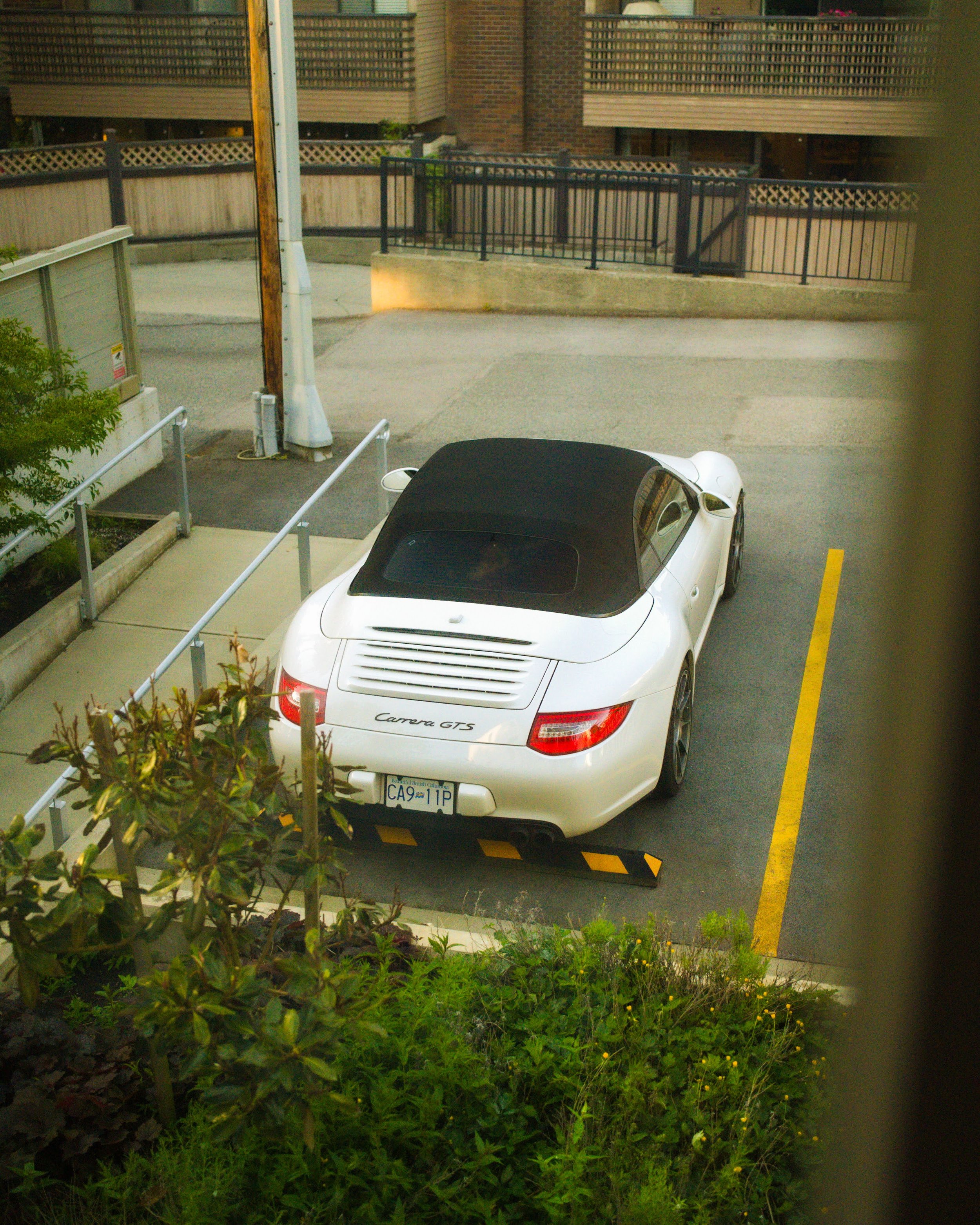A white Porsche Carrera GTS convertible with a black soft top, parked in an outdoor parking lot with yellow painted lines.