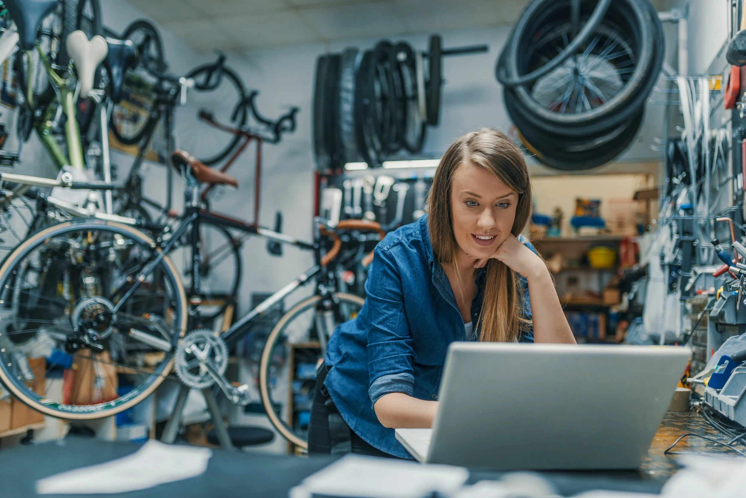 Image shows small business owner in their repair shop looking at a computer and smiling