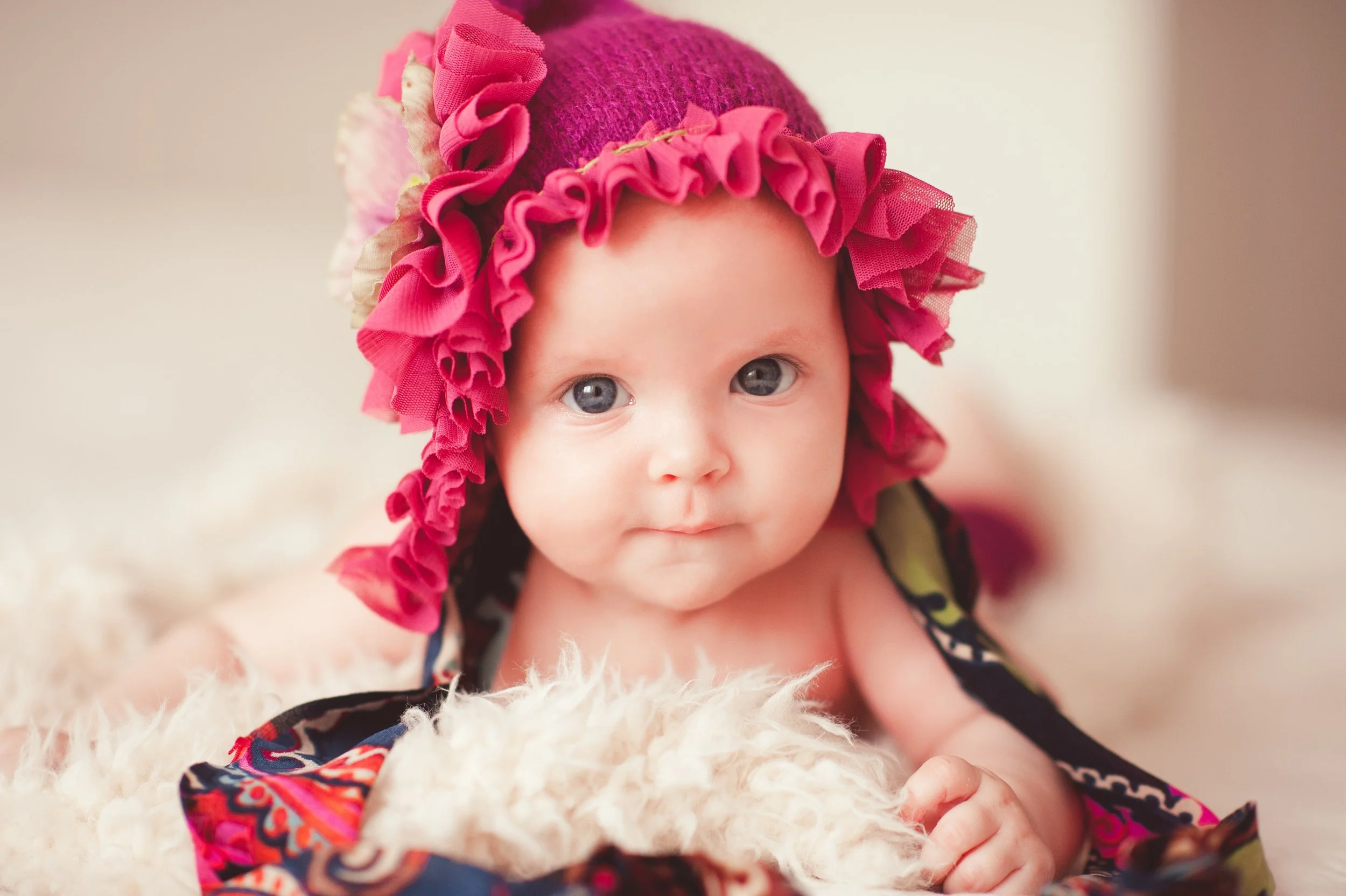 Close-up of a baby wearing a pink hat with ruffles, lying on a soft, fuzzy blanket.