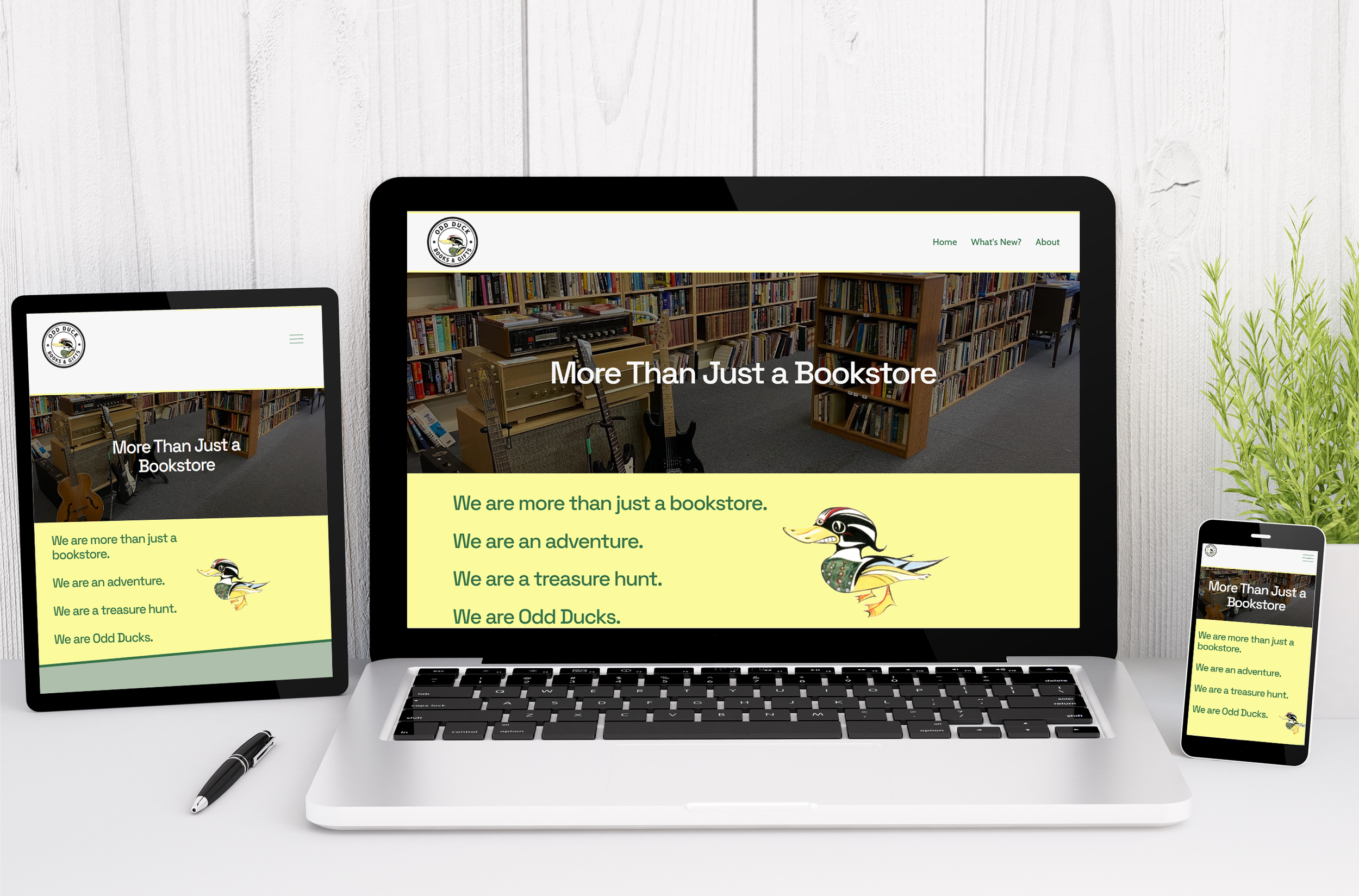 A laptop, tablet, and mobile phone showing scaled versions of a website for Odd Ducks Bookstore, on a clean, white desk setting with a pen and a plant nearby.