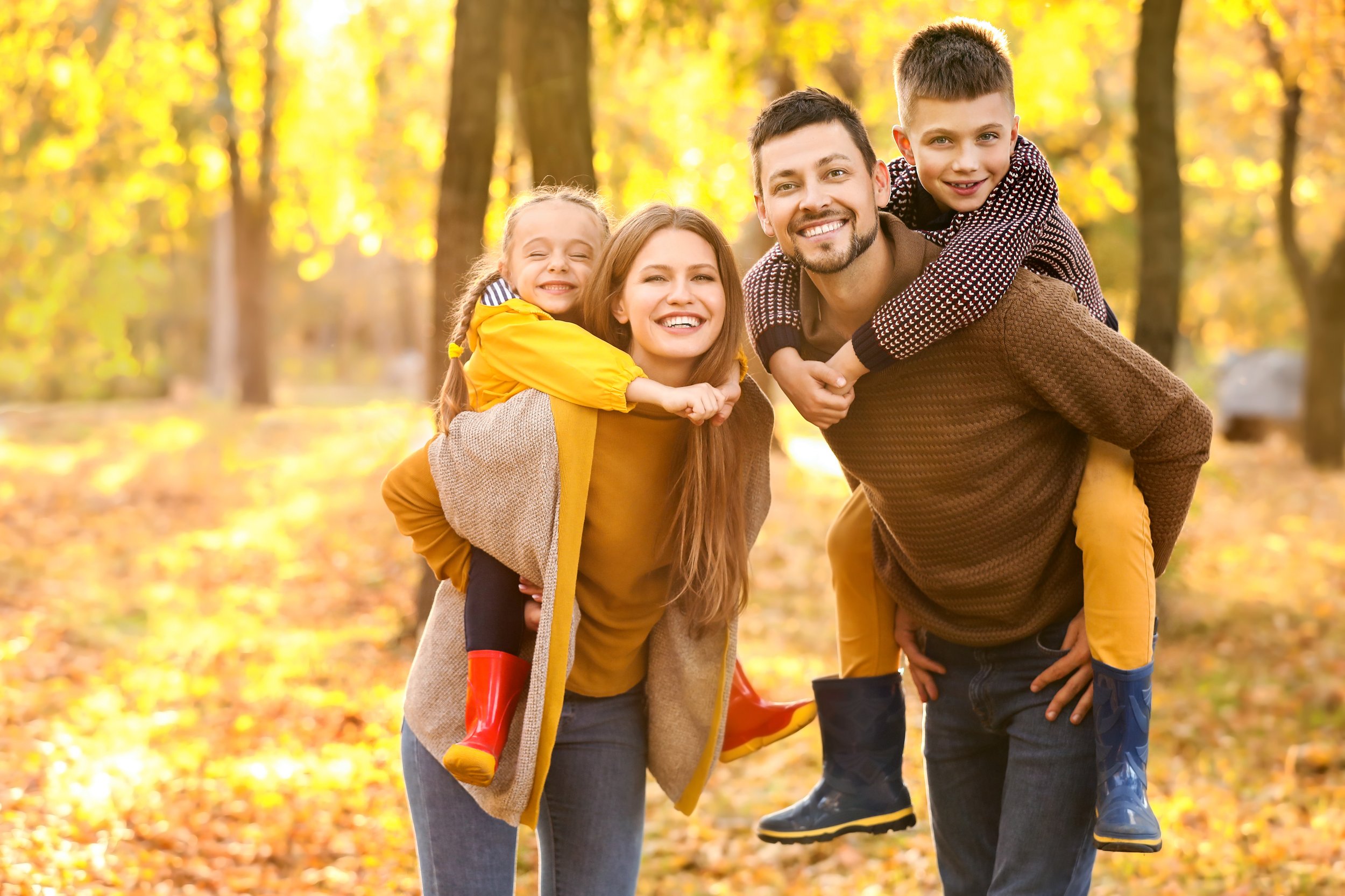A happy family enjoying a walk in the autumn park with yellow leaves on the ground and trees.