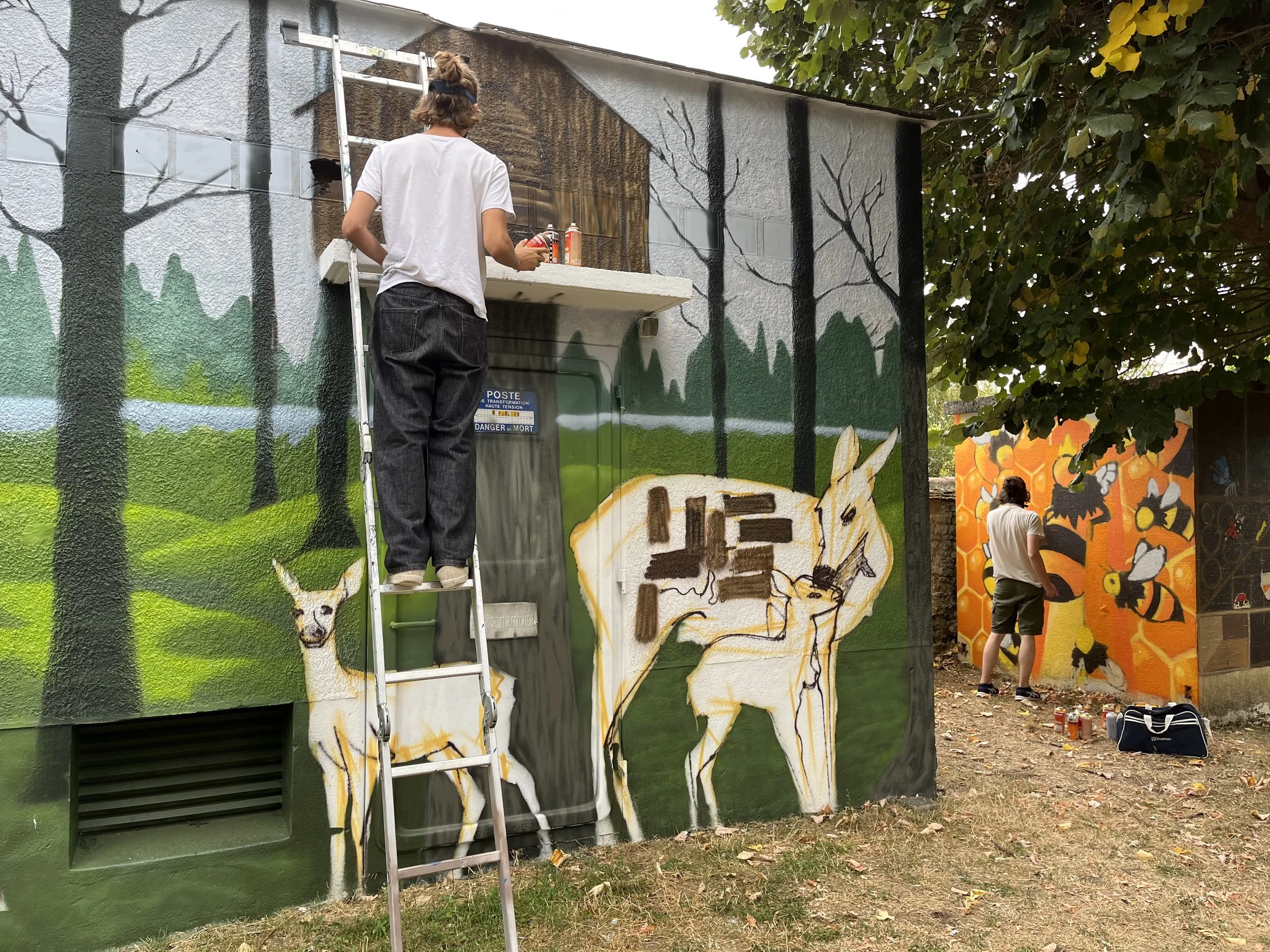 fresque murale participative représentant une forêt avec des arbres et des animaux, sous un arbre avec des feuilles vertes.