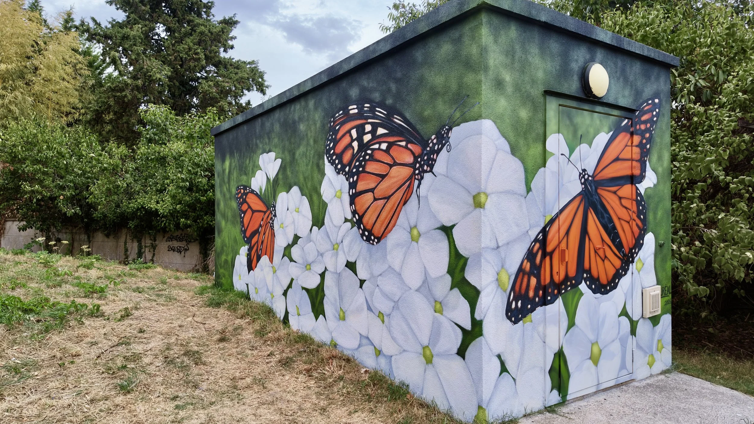 Vue latérale d'un transformateur électrique décoré d'une peinture murale de papillons monarques et de végétation à Moret-Loing-et-Orvanne.
