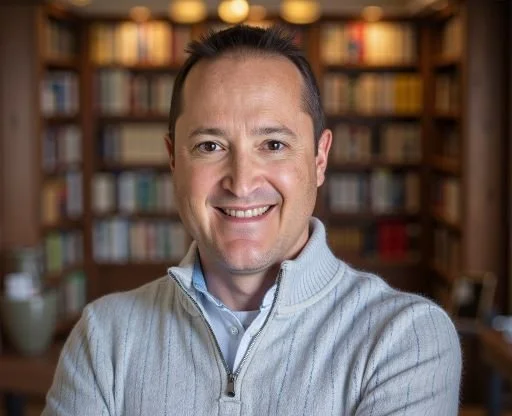 A man smiling in front of a bookshelf filled with books.