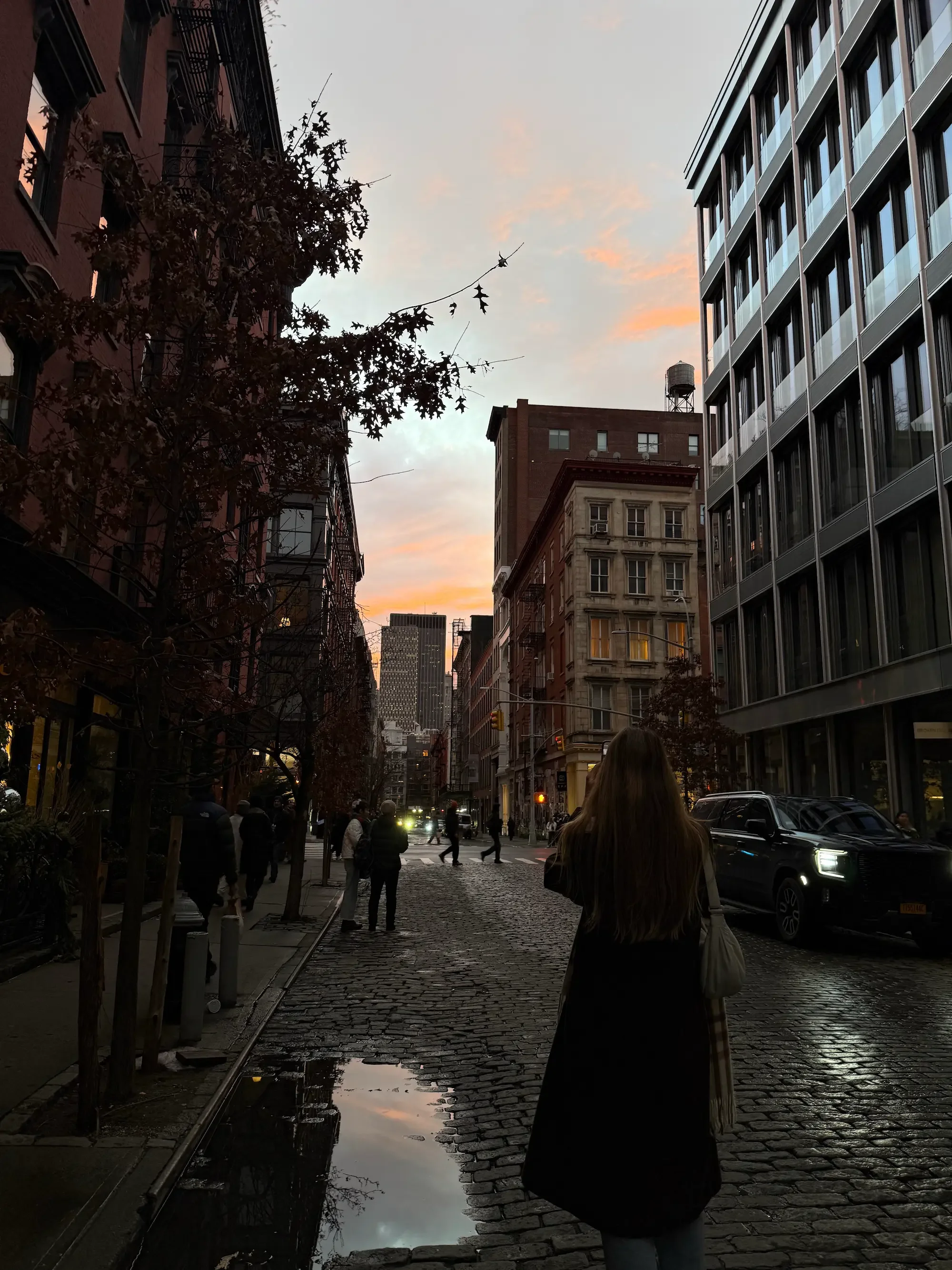 Woman walking alone on a cobblestone street at sunset in New York City, reflecting a thoughtful moment in therapy