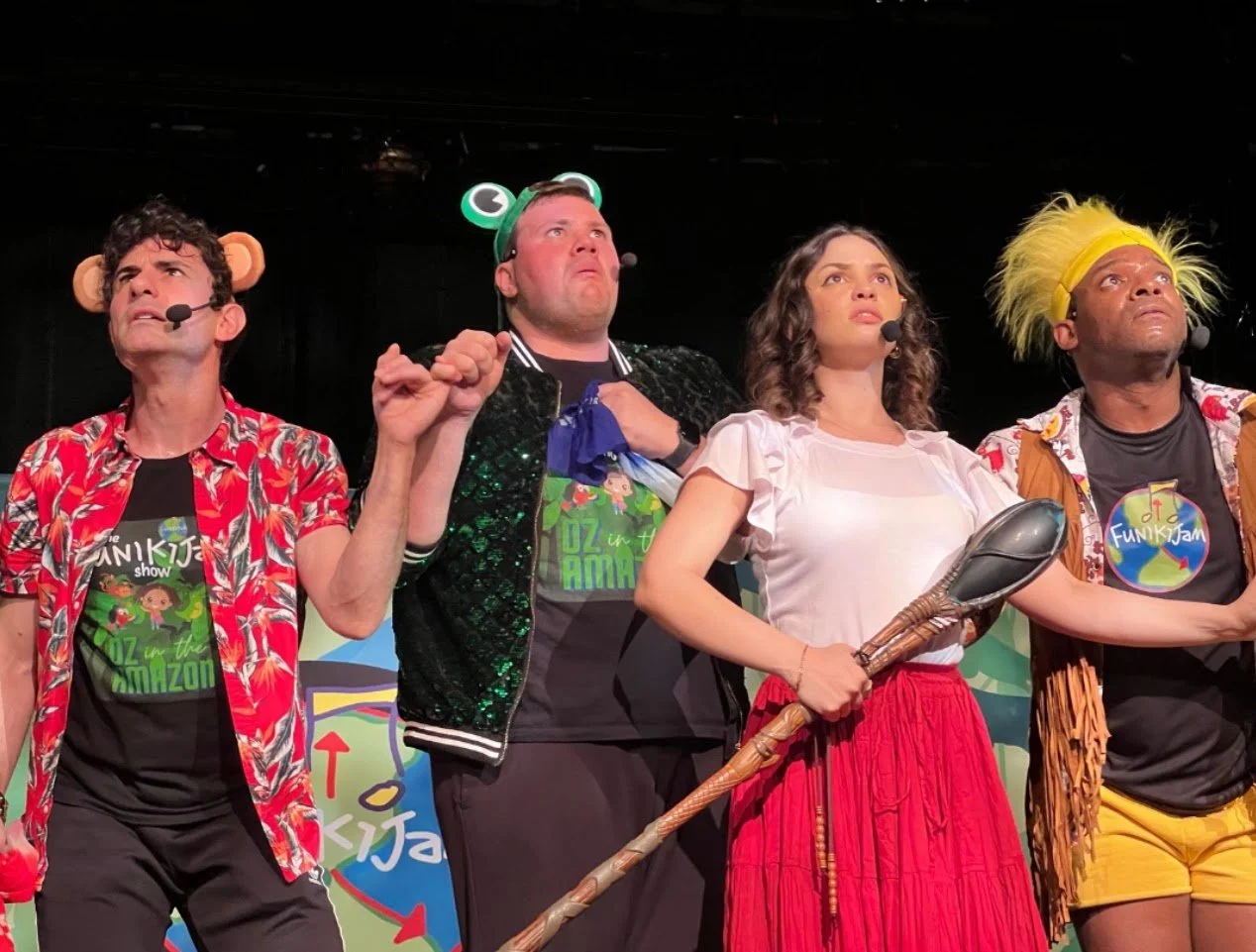 Four performers on stage dressed in colorful costumes with animal and nature-themed accessories.