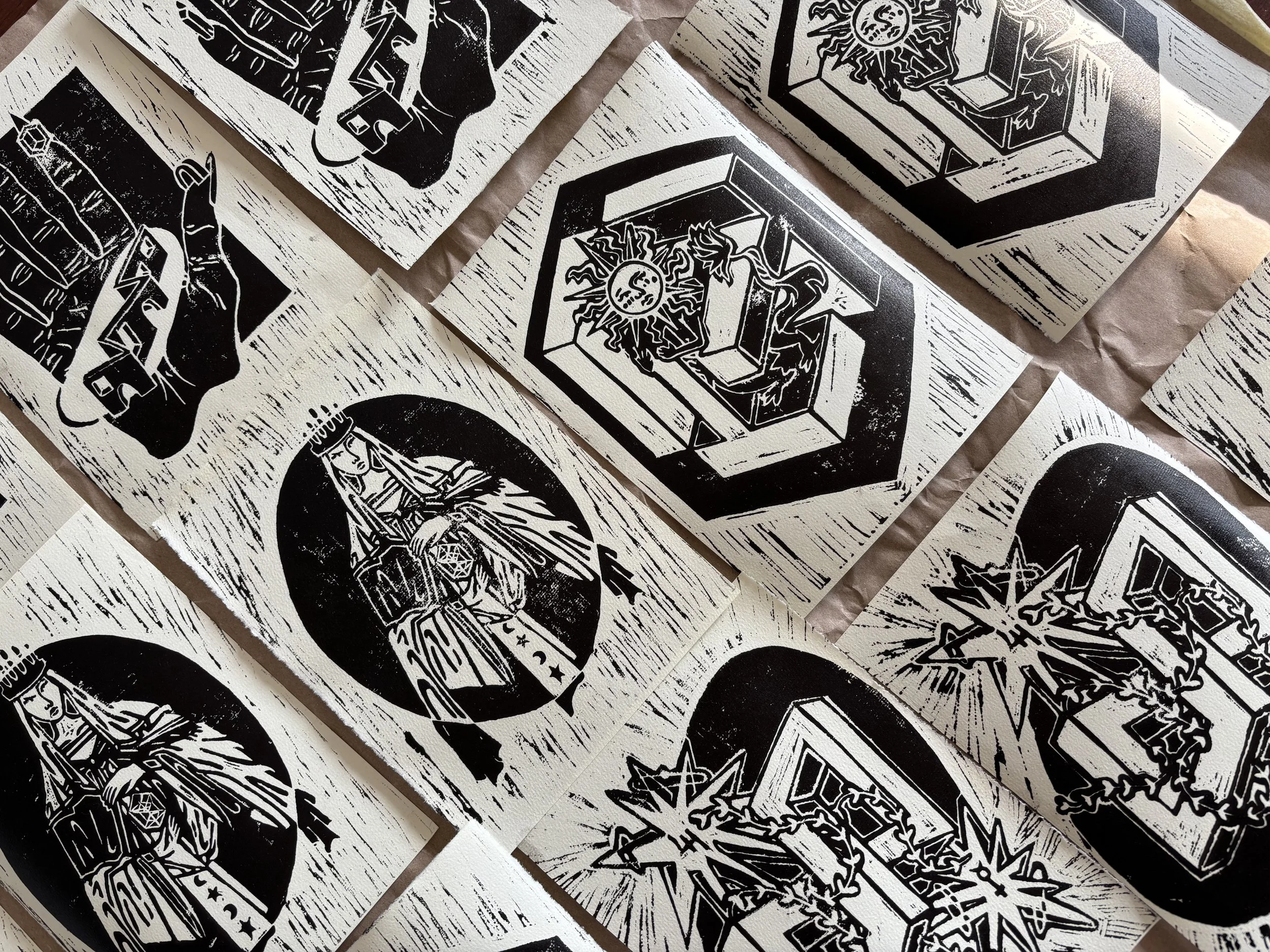 Black and white linocut art prints of varied symbolic and religious imagery, including a depiction of the Virgin Mary, mystical symbols, and geometric designs, arranged on a flat surface.