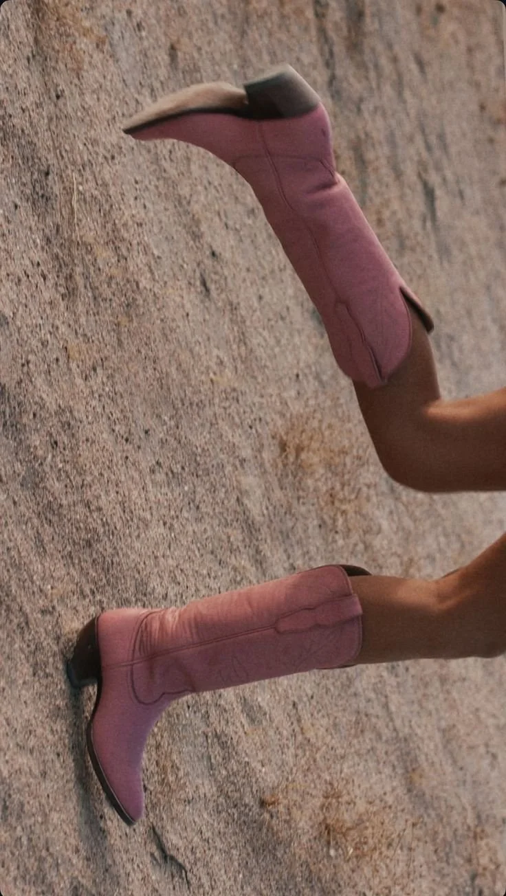 Person wearing pink cowboy boots standing on dirt ground.