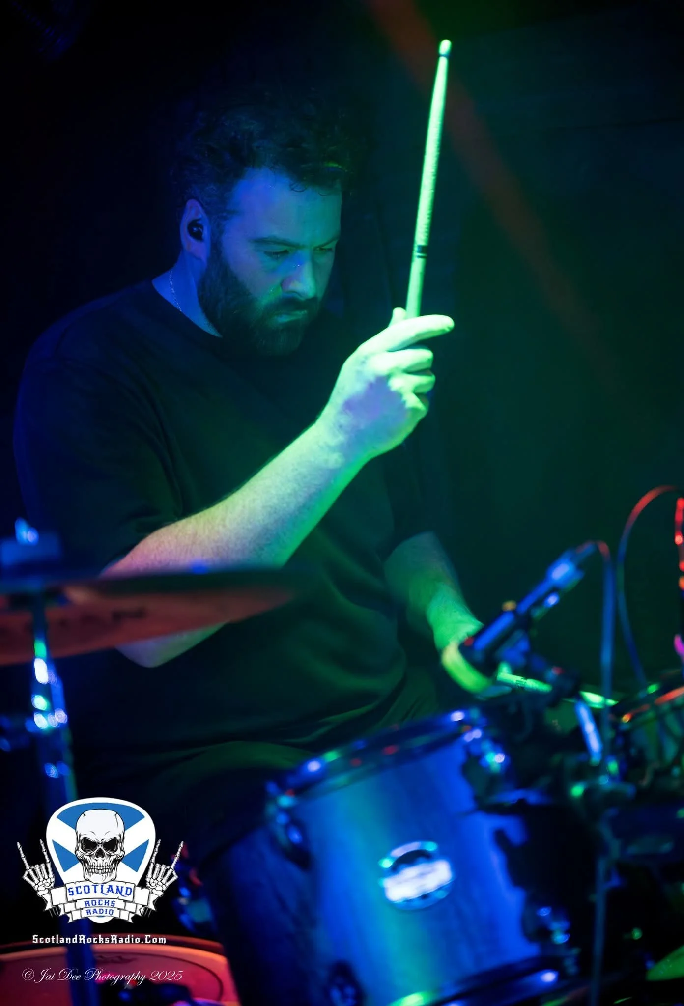 SOMB Scared of My Brother Arthur Kinnear-Kirkwood playing drums in a dark room illuminated by green and purple stage lights, with a logo for Scotland Rocks Radio at the bottom left corner.