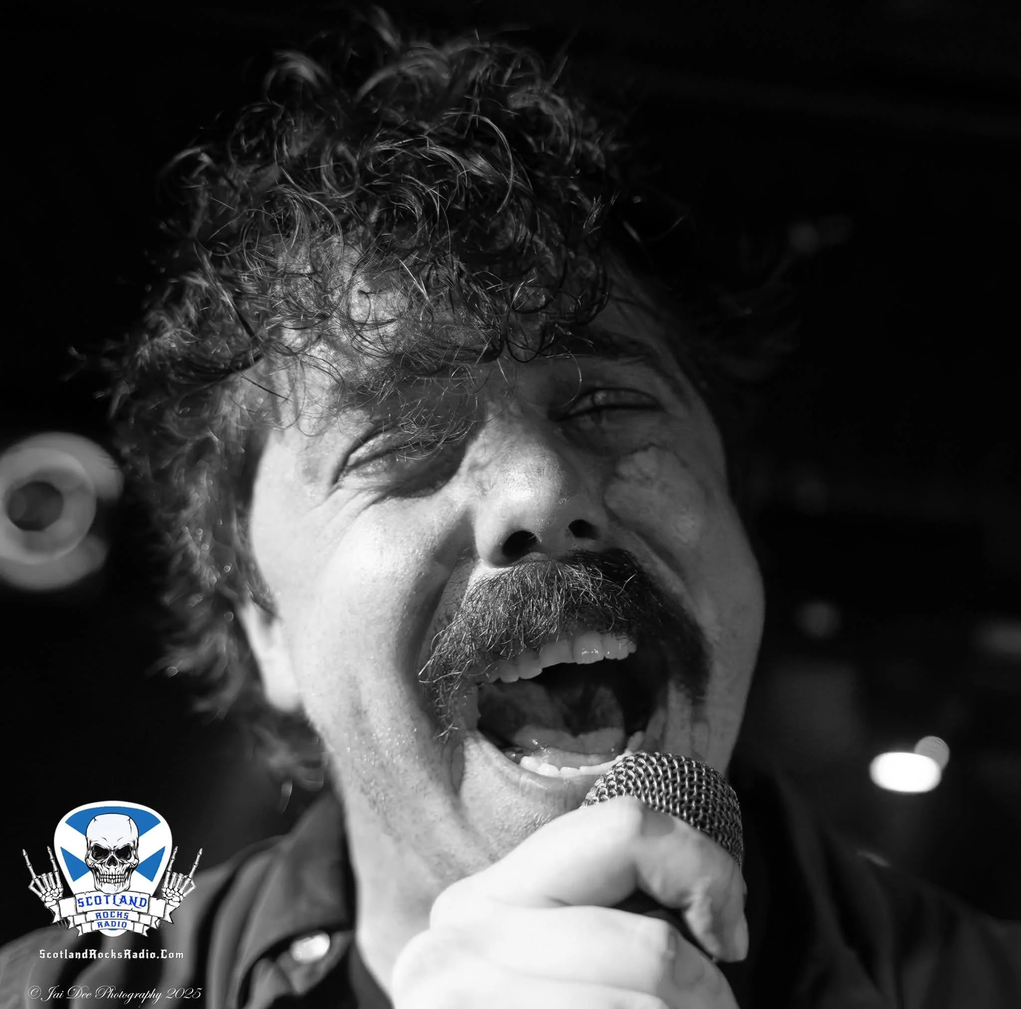 SOMB Scared of My Brother lead singer (Lewis Thomson) singing into a microphone. There is a logo in the bottom left corner that features a skull with headphones and the text "Scotland Rocks Radio".