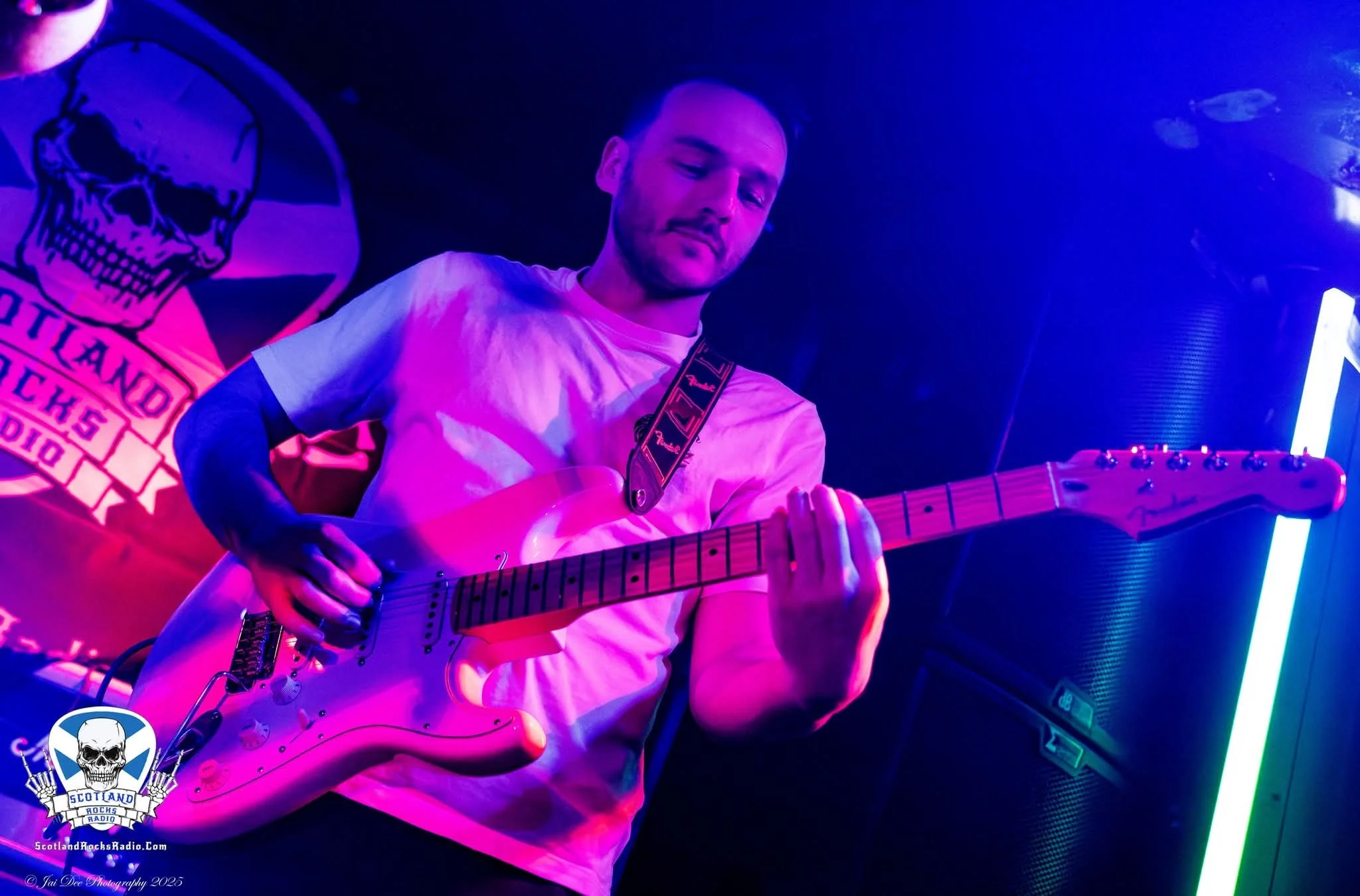 SOMB Scared of My Brother Lead Guitarist Tom Cartwright plays an electric guitar on stage with purple and blue lighting.