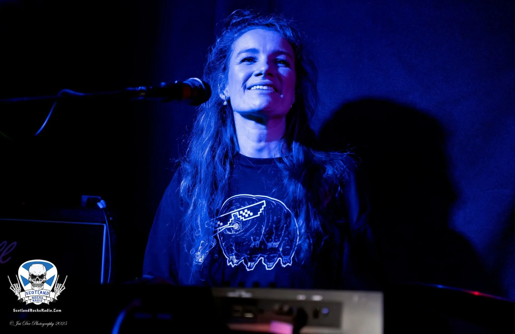 SOMB Scared of My Brother Keyboard player Phoebe Russell singing. There is a logo in the bottom left corner that says 'Scotland Rocks Radio,' featuring a skull and two hands making rock signs.