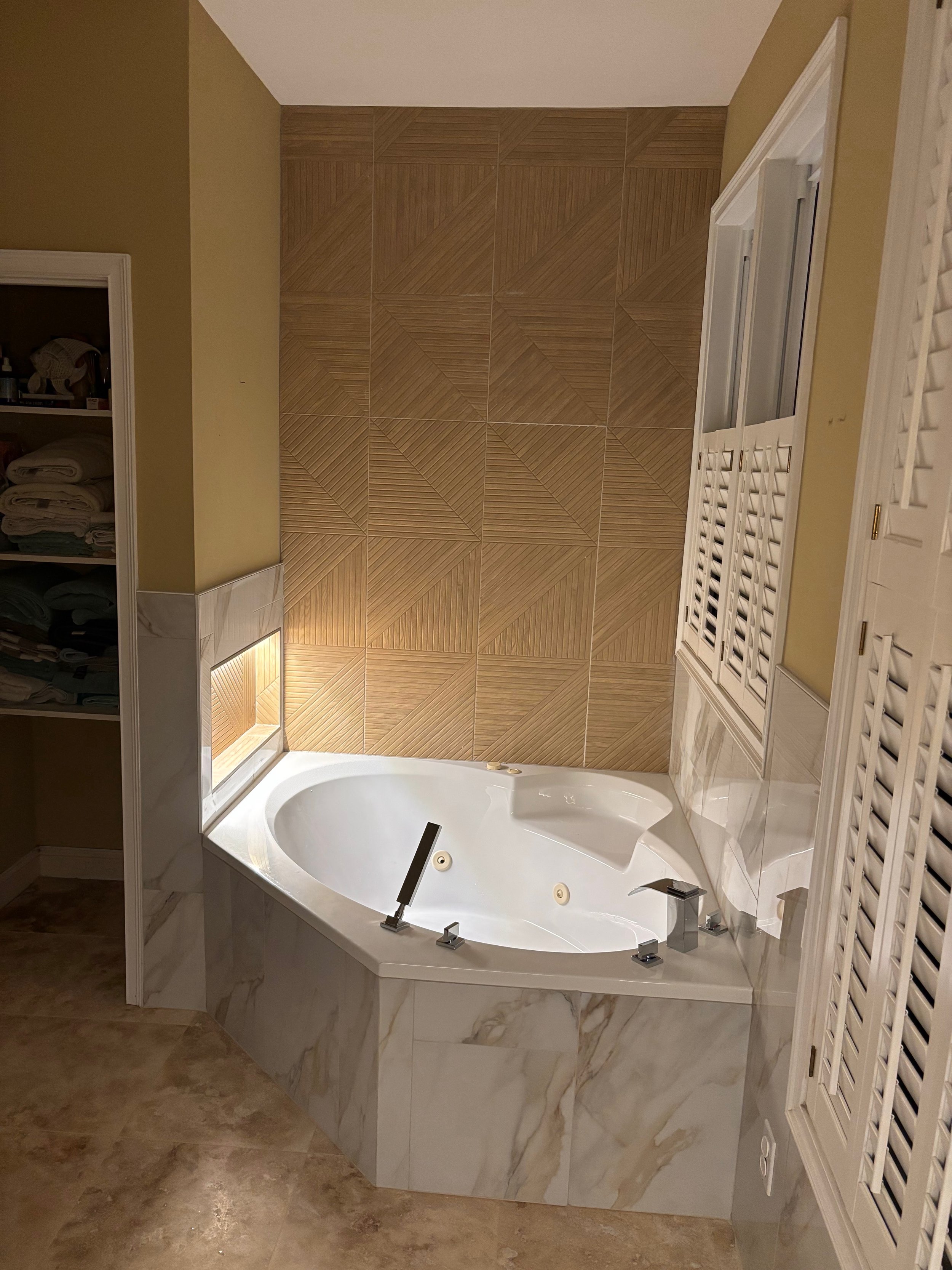 A bathroom featuring a corner whirlpool bathtub with a marble base, beige tile walls with a geometric pattern, and a white louvered cabinet or radiator on the right side.