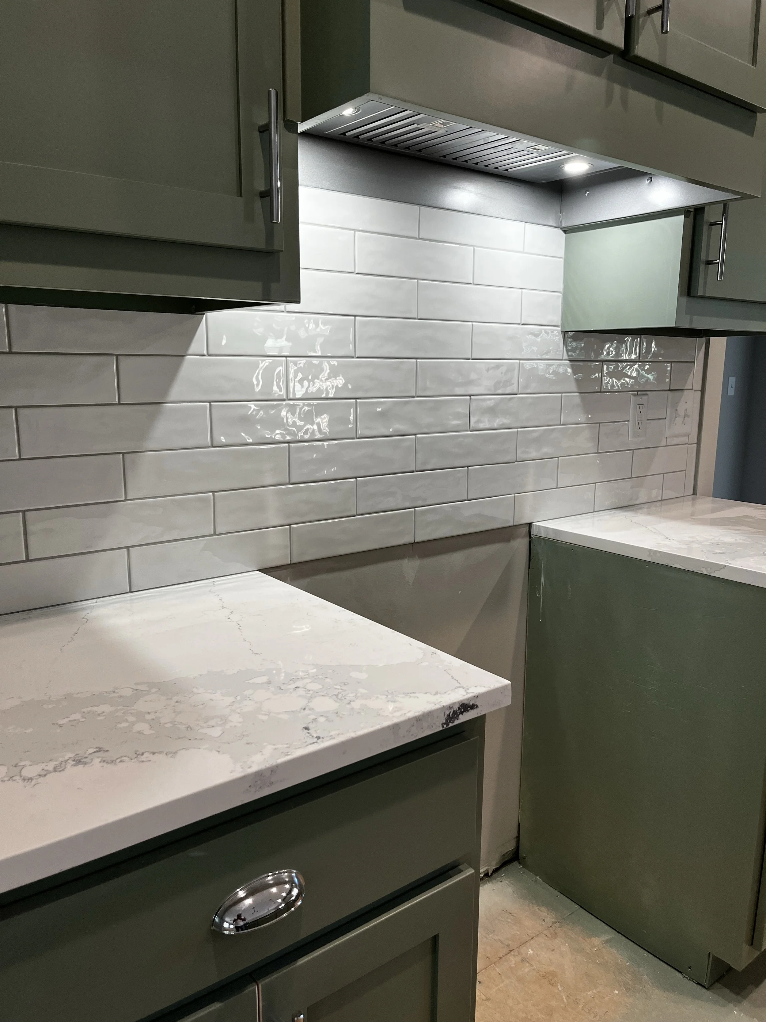 Modern kitchen with white marble countertop, green cabinets, white subway tile backsplash, and a built-in exhaust fan under upper cabinets.