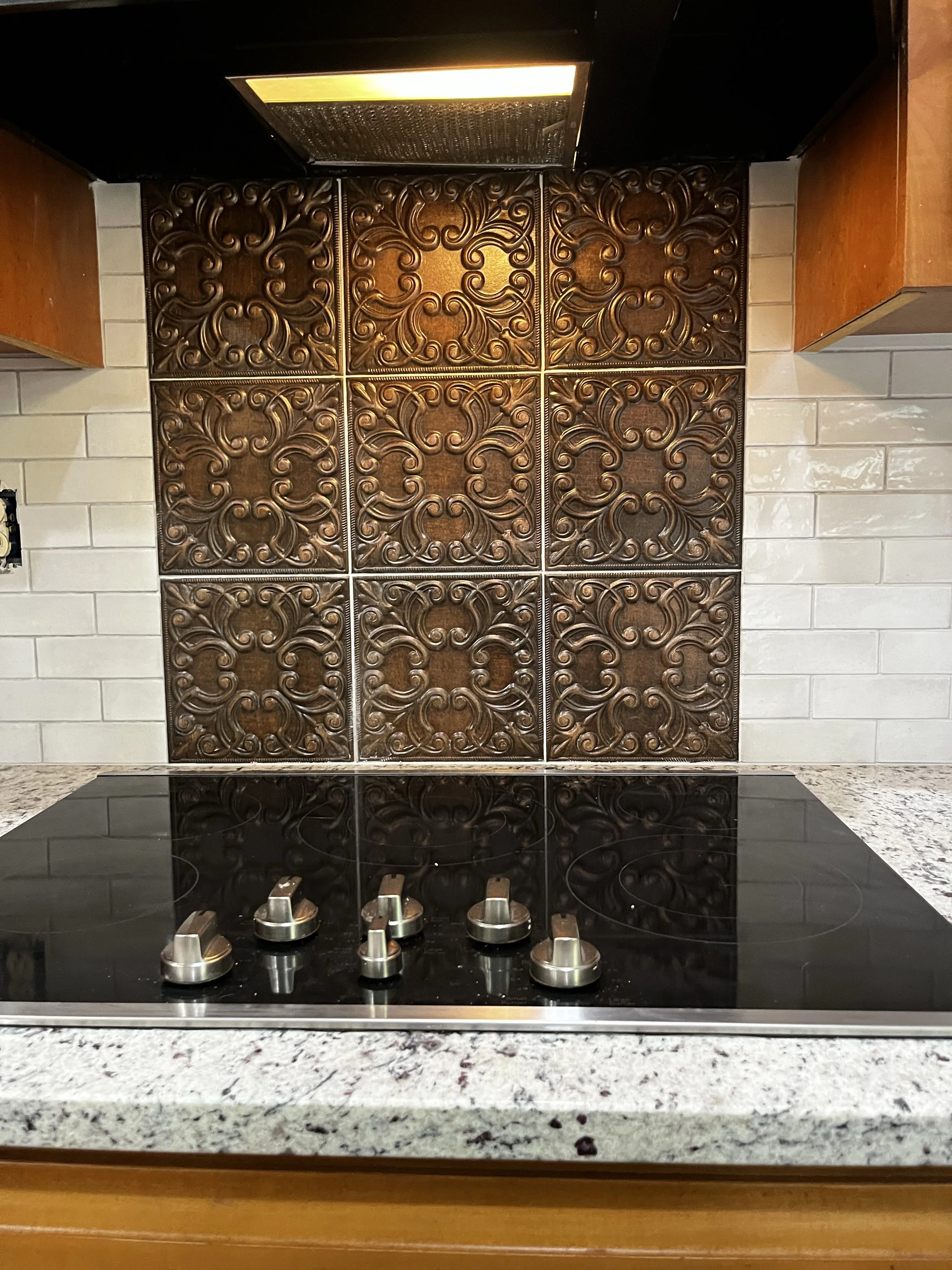 Custom kitchen backsplash featuring ornate, bronze-toned decorative tiles framed by classic white subway tiles, creating an elegant focal point above the stovetop.