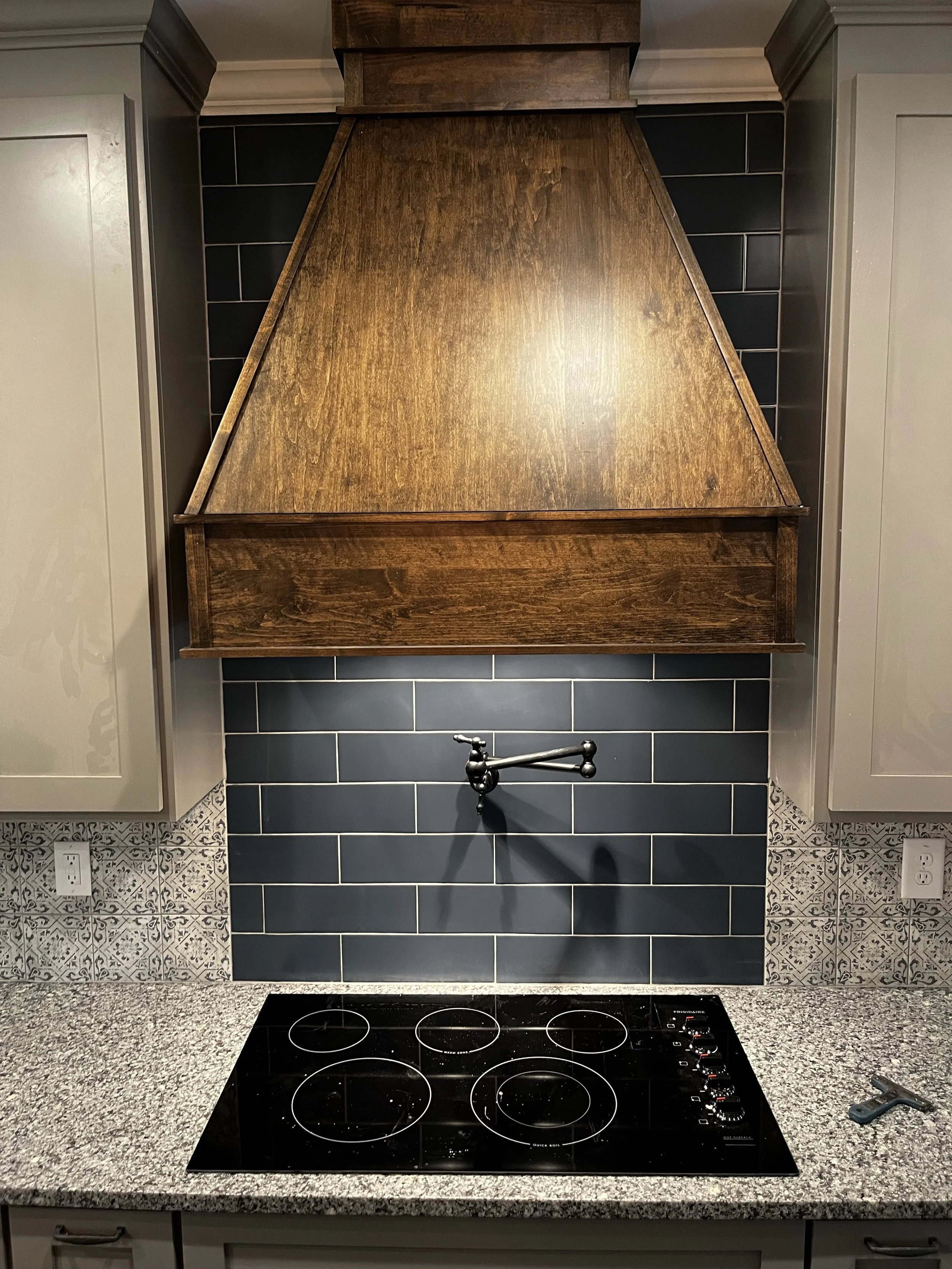 Custom kitchen backsplash featuring sleek black subway tiles with contrasting light grout, beautifully complementing the rustic wood range hood and patterned accent tiles.