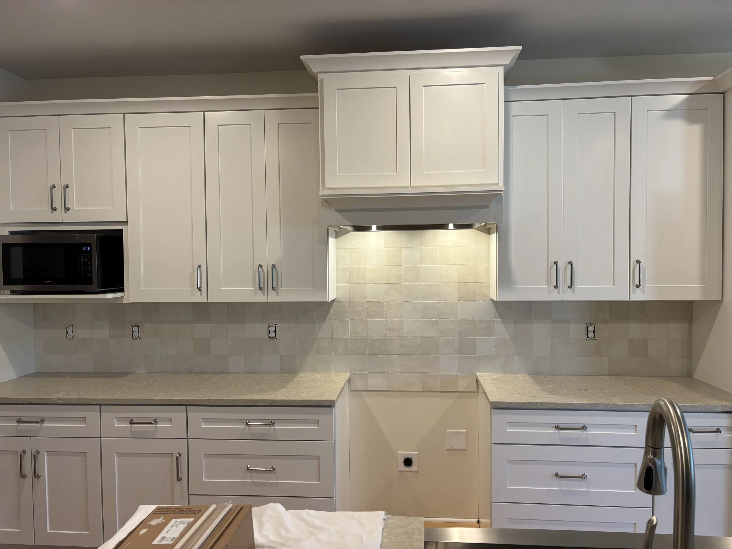 Kitchen with white cabinets, beige countertops, built-in microwave, and tiled backsplash.