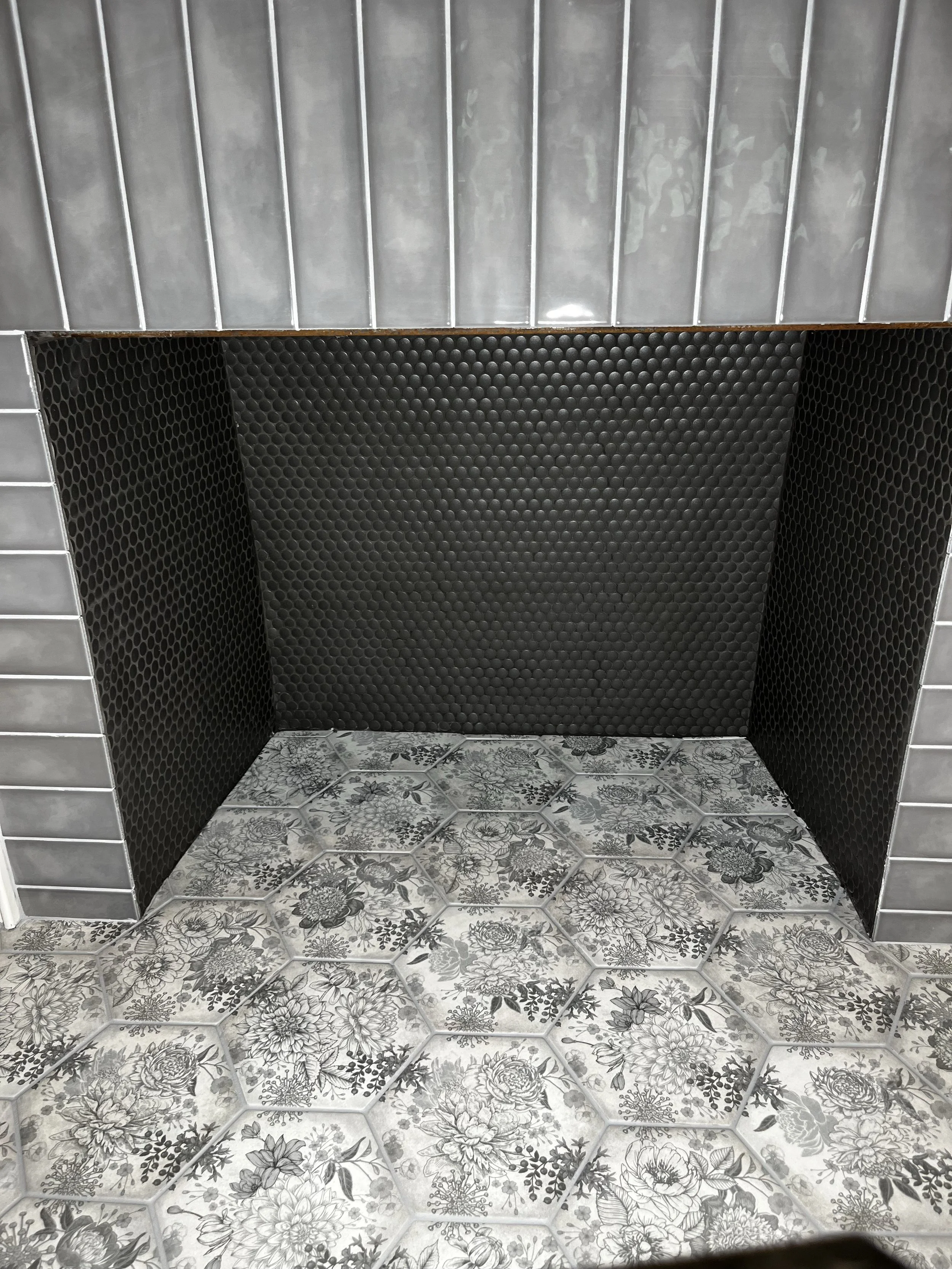 Part of an outdoor enclosed shower with floral tile floor, black honeycomb tiles on the walls, and gray tiles on the sides.